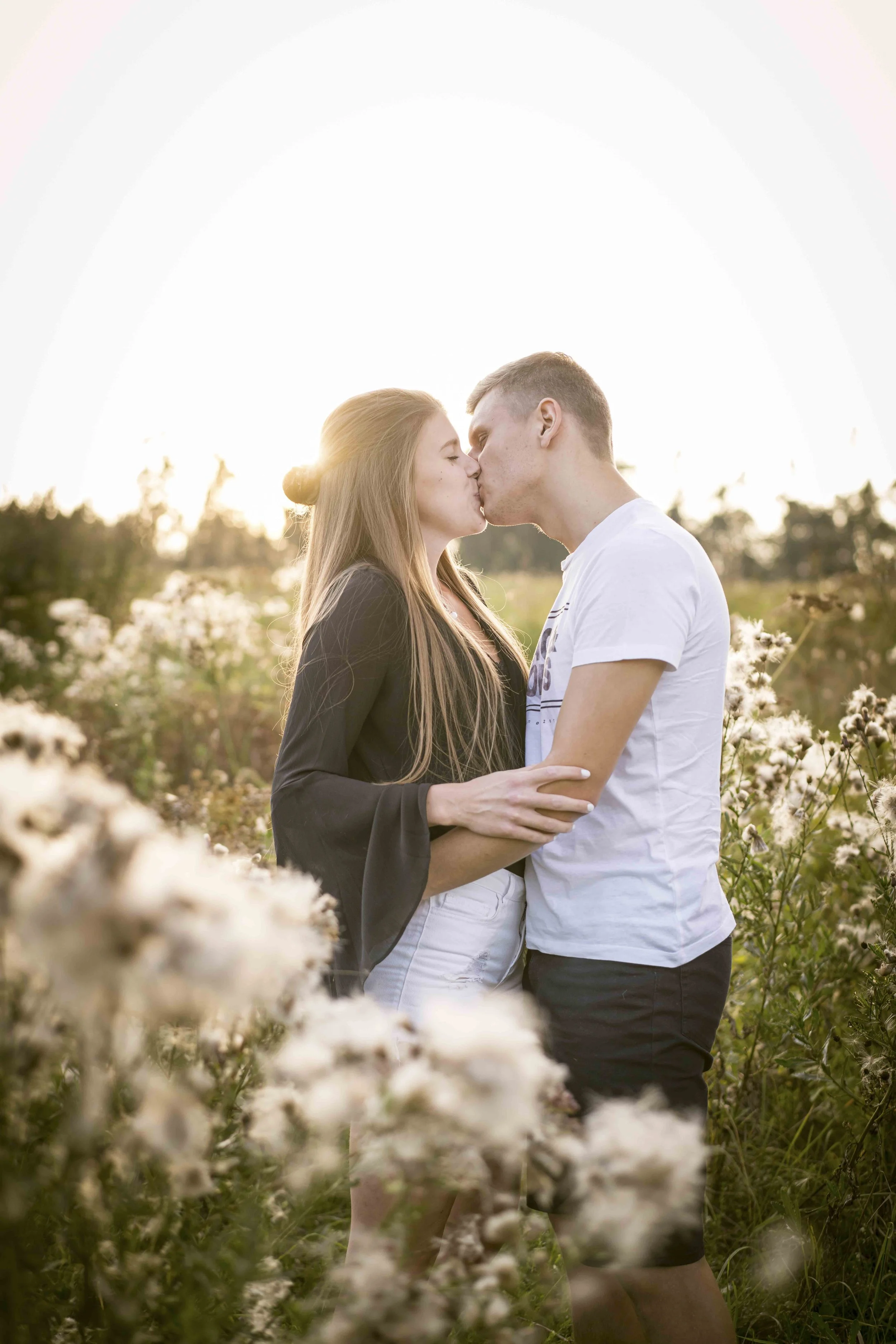 Ein Paar küsst sich in einem blühenden Feld bei Sonnenuntergang.
