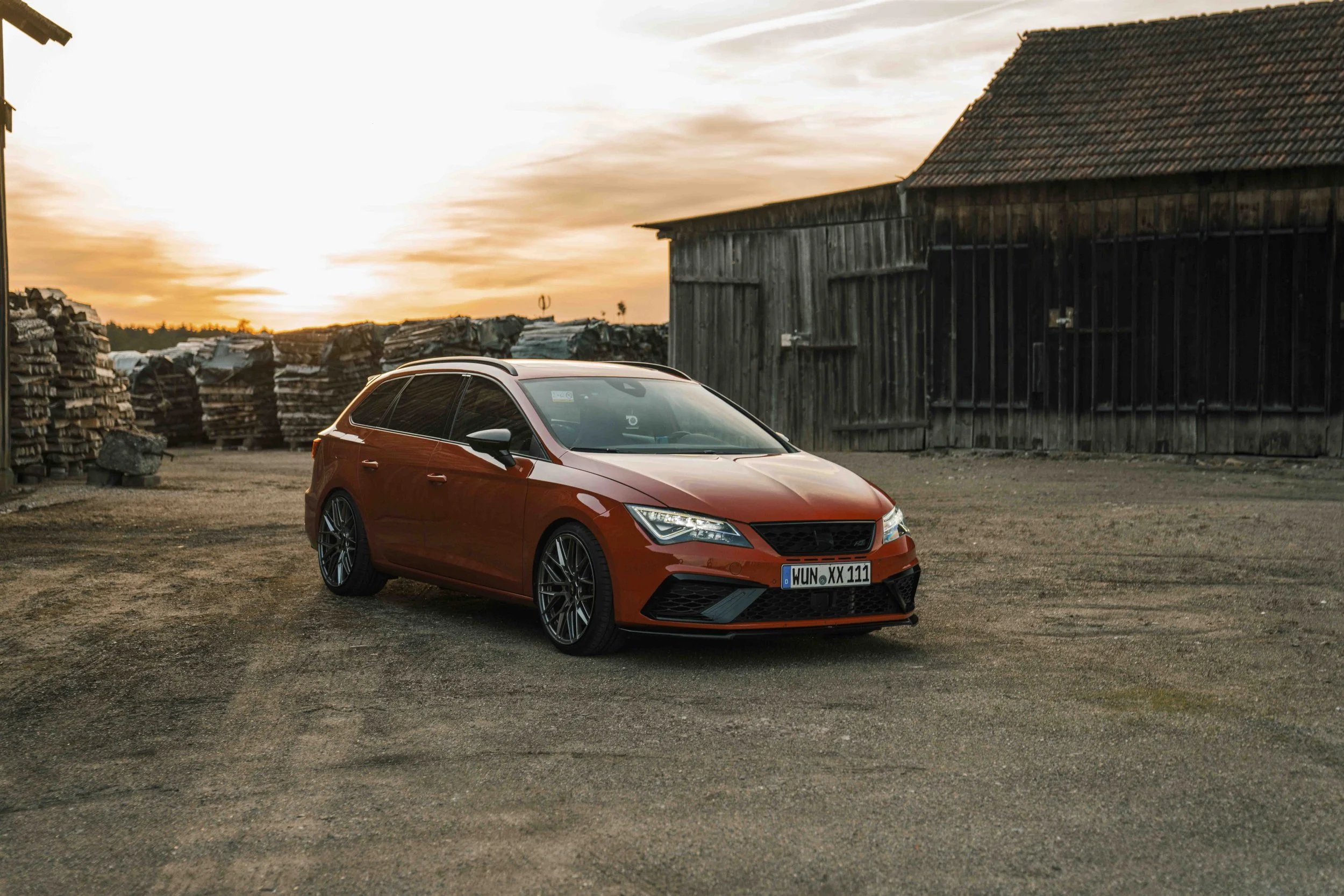 Rotes Auto vor einer Scheune bei Sonnenuntergang.