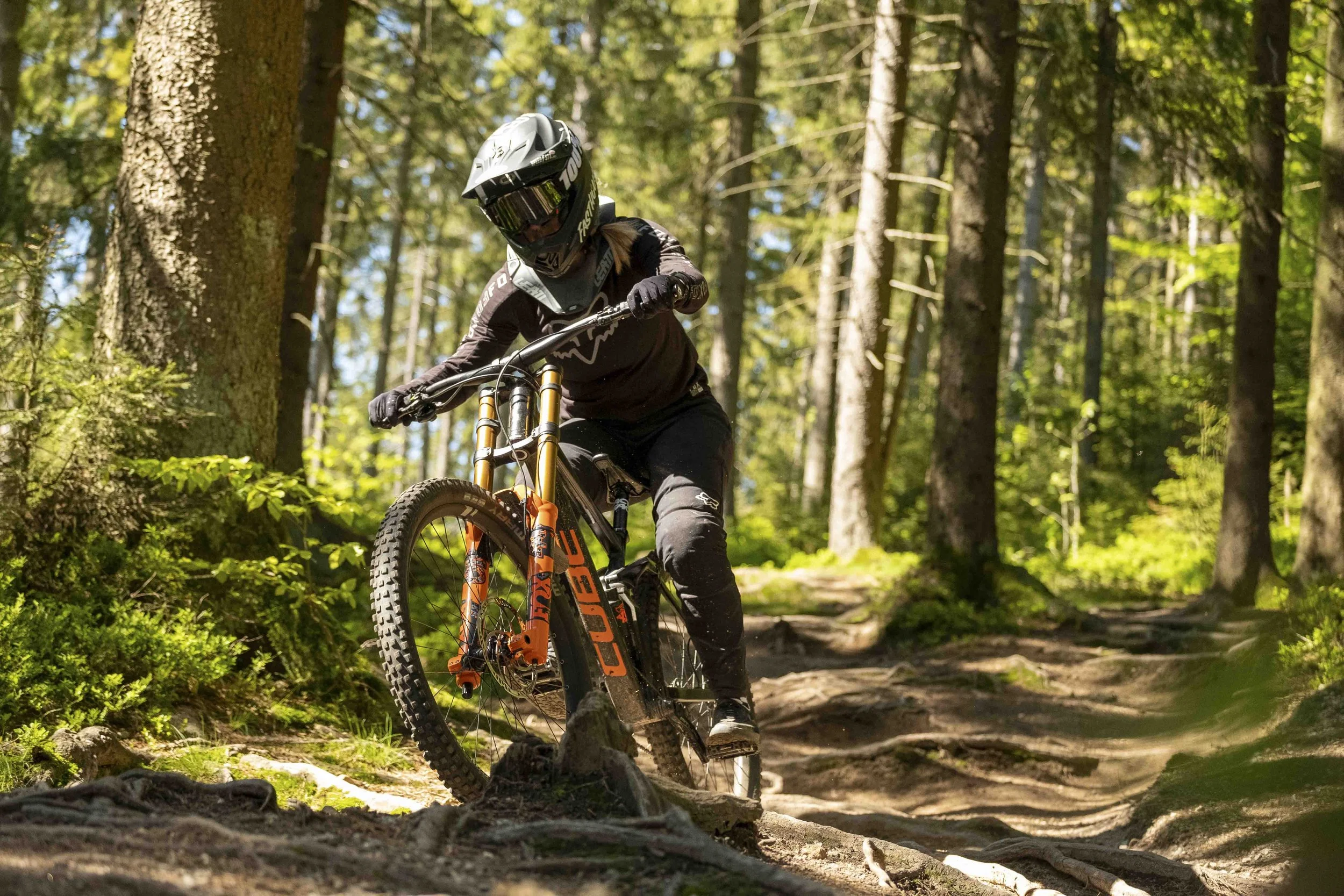 Mountainbiker im Wald auf einem steinigen Pfad, trägt Helm und Schutzkleidung, fahrradfahrend in einer natürlichen, bewaldeten Umgebung.