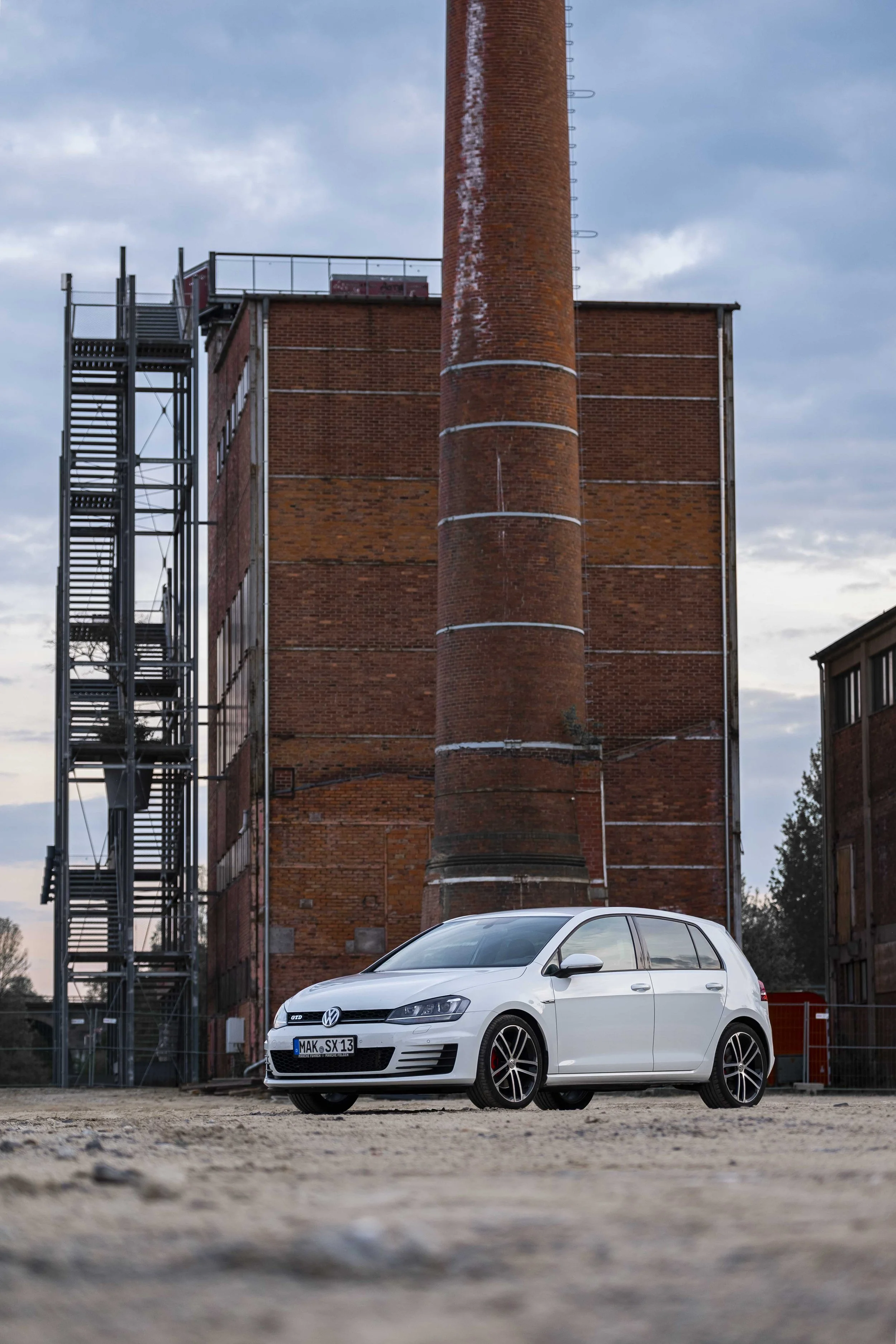 Weißes Auto vor einem Industriegebäude mit Schornstein und Treppe.