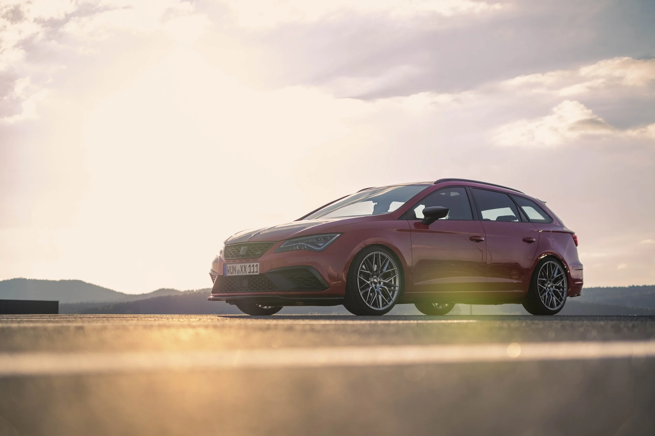 Rotes Auto auf offener Straße bei Sonnenuntergang, mit Bergen im Hintergrund.