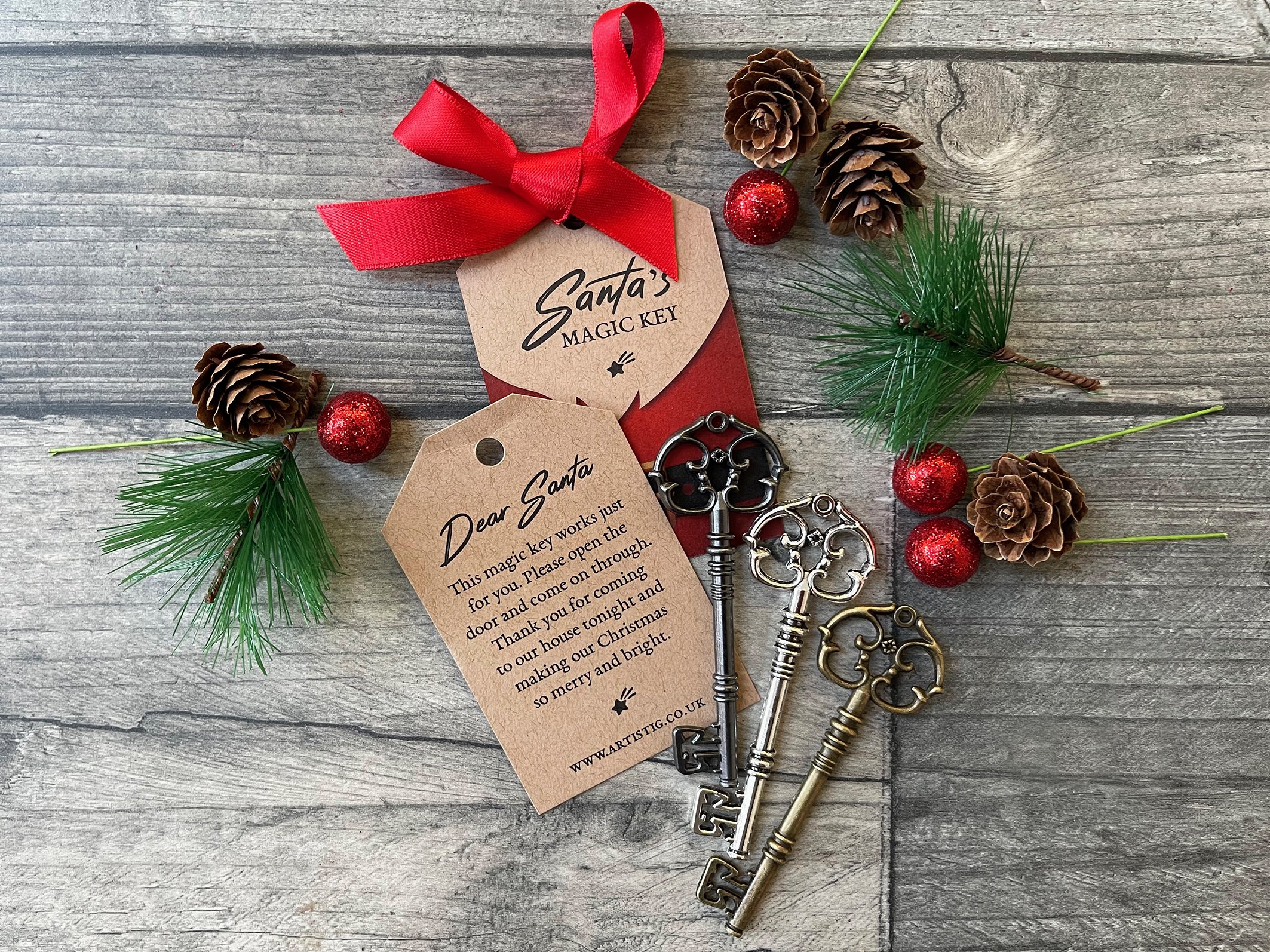Christmas-themed display featuring three vintage keys labeled 'Santa’s Magic Key' with decorative pinecones, red baubles, green pine branches, and a red ribbon on a wooden background.