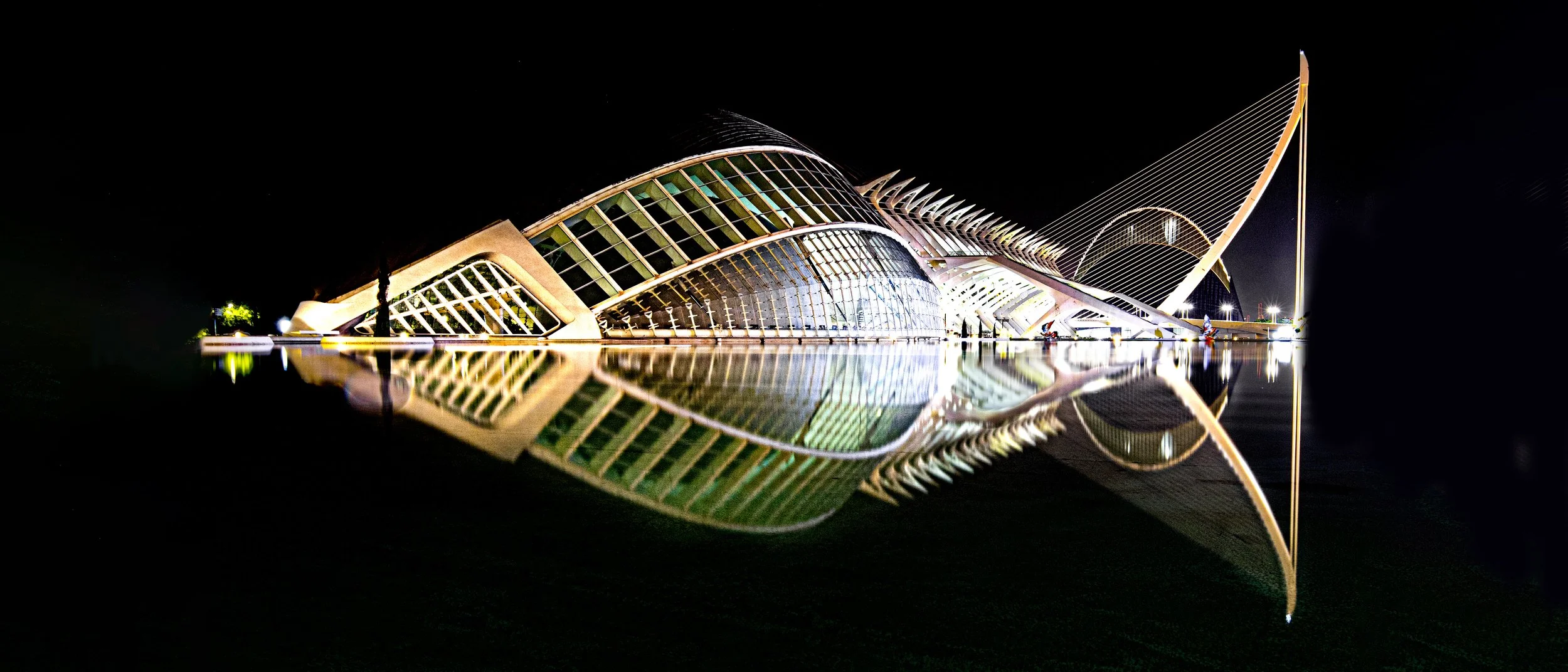 Night view of the modern, illuminated musical instrument museum with a glass facade and structural elements reflecting on the water.