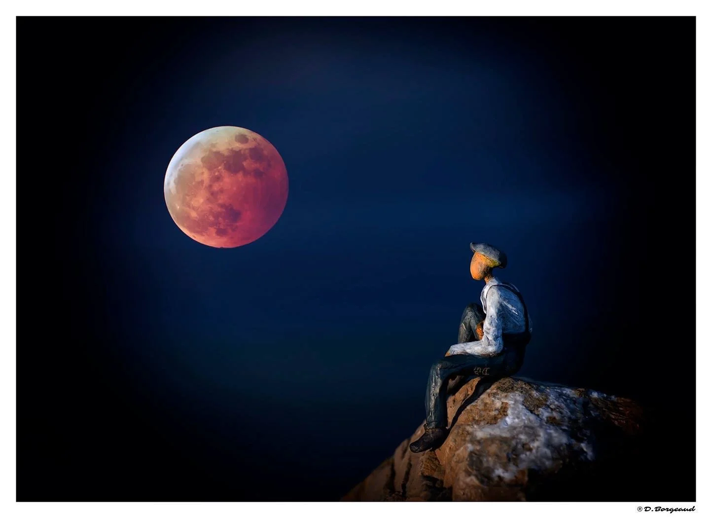A person with a painted face and hat sitting on a rock, gazing at a large, reddish lunar eclipse in a dark sky.