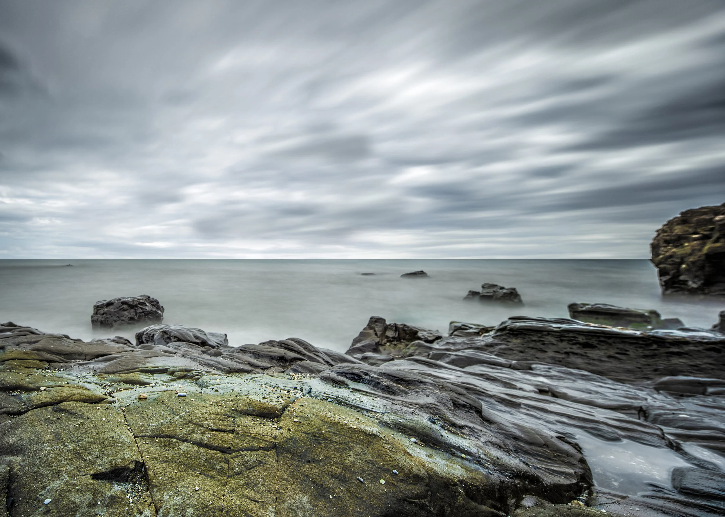Overcast sky with moving clouds over a rocky shoreline and calm ocean water.