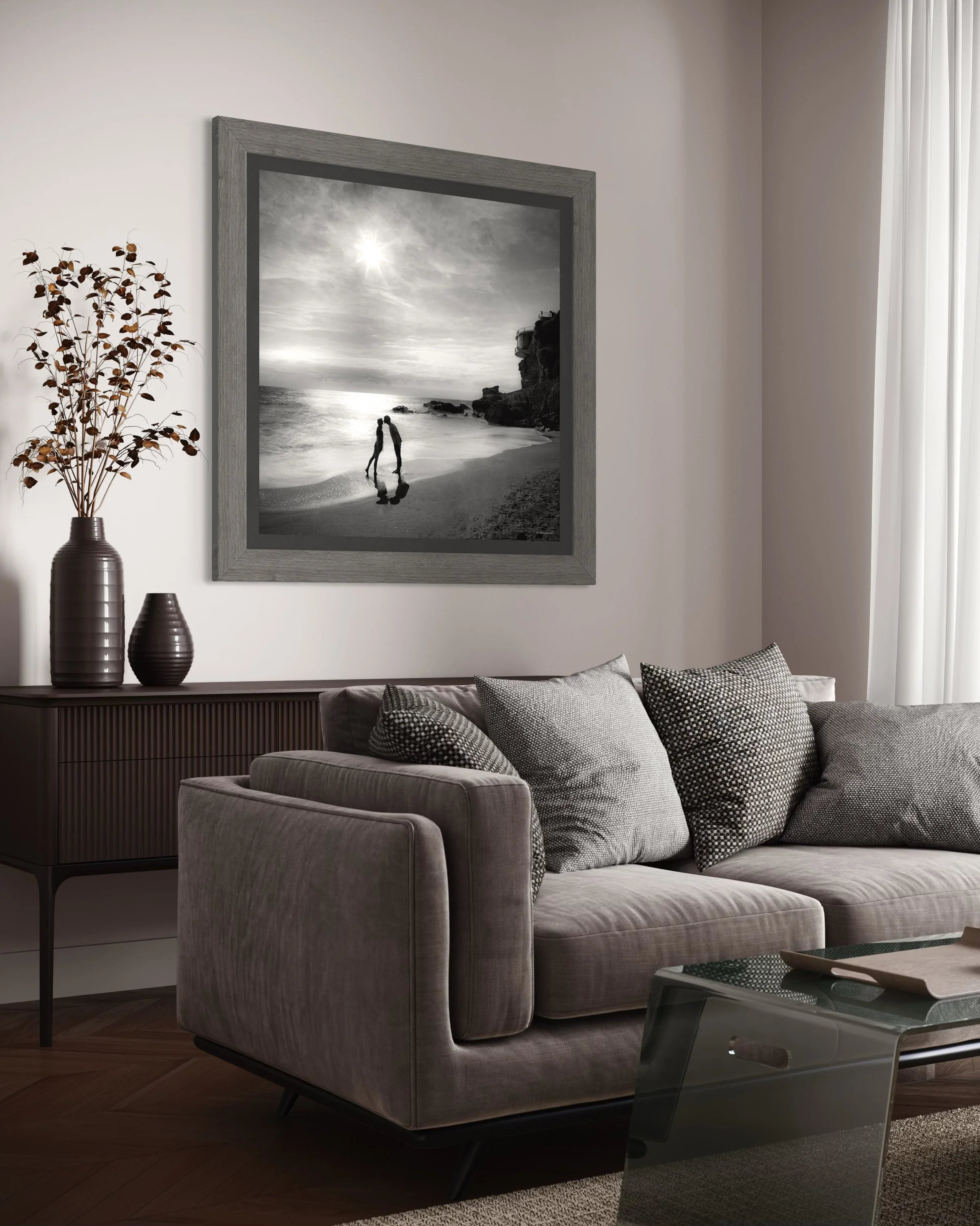 A living room with a gray sofa, black and white decorative pillows, a wooden sideboard with vases, and a black and white beach photograph on the wall.