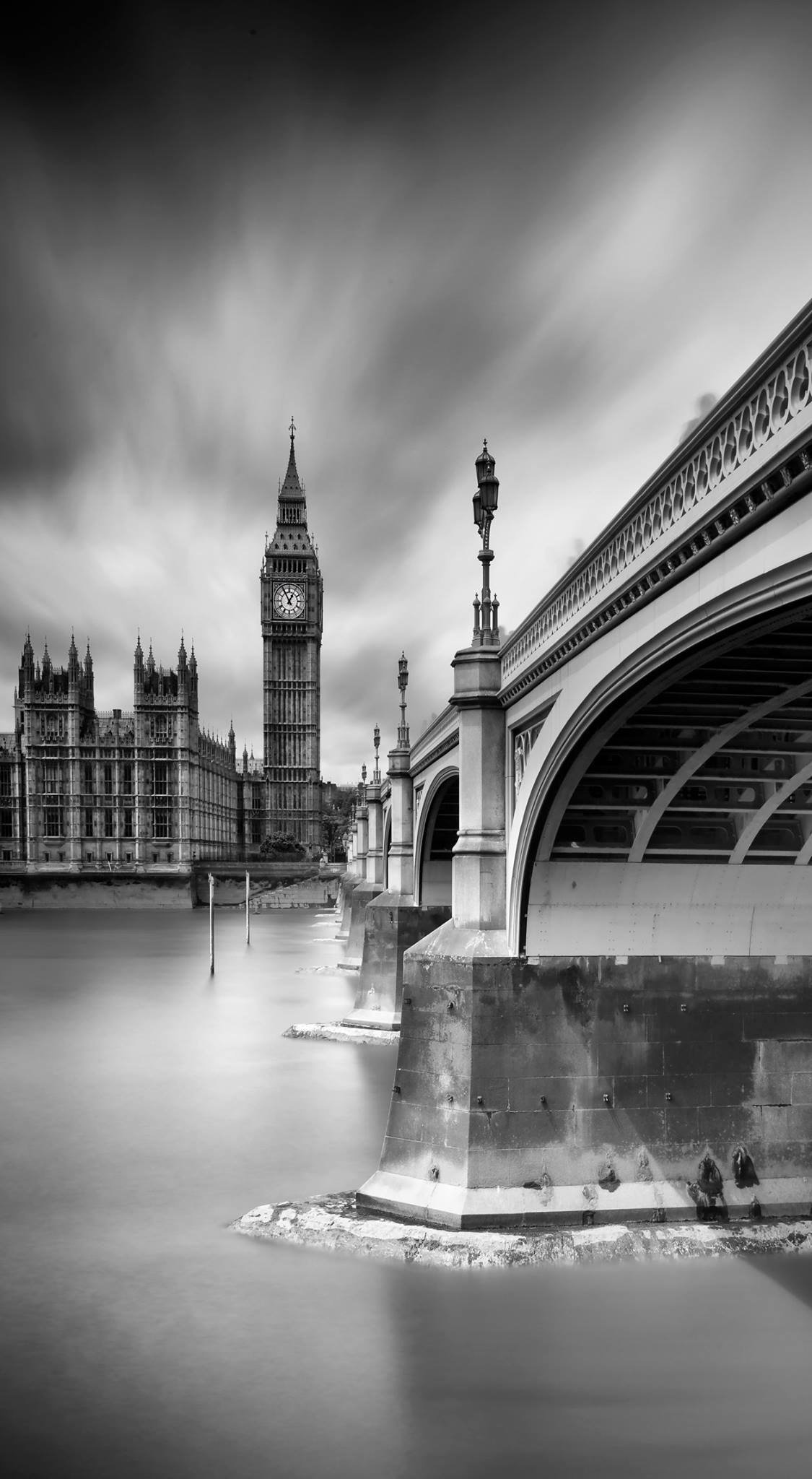 Black and white photo of the Houses of Parliament and Big Ben in London, with Westminster Bridge in the foreground and no visible people.