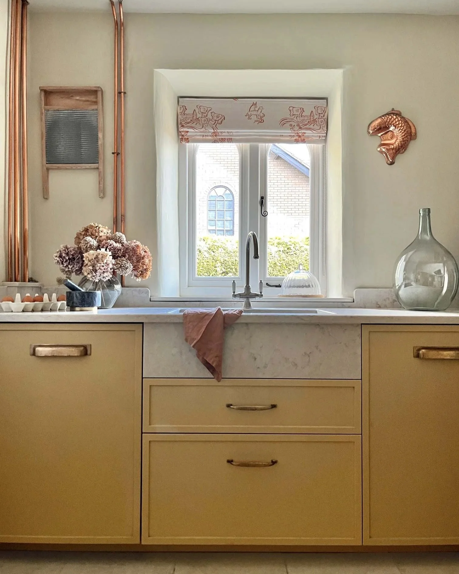 yellow pantry cabinets with antique brass handles andsink in front of window