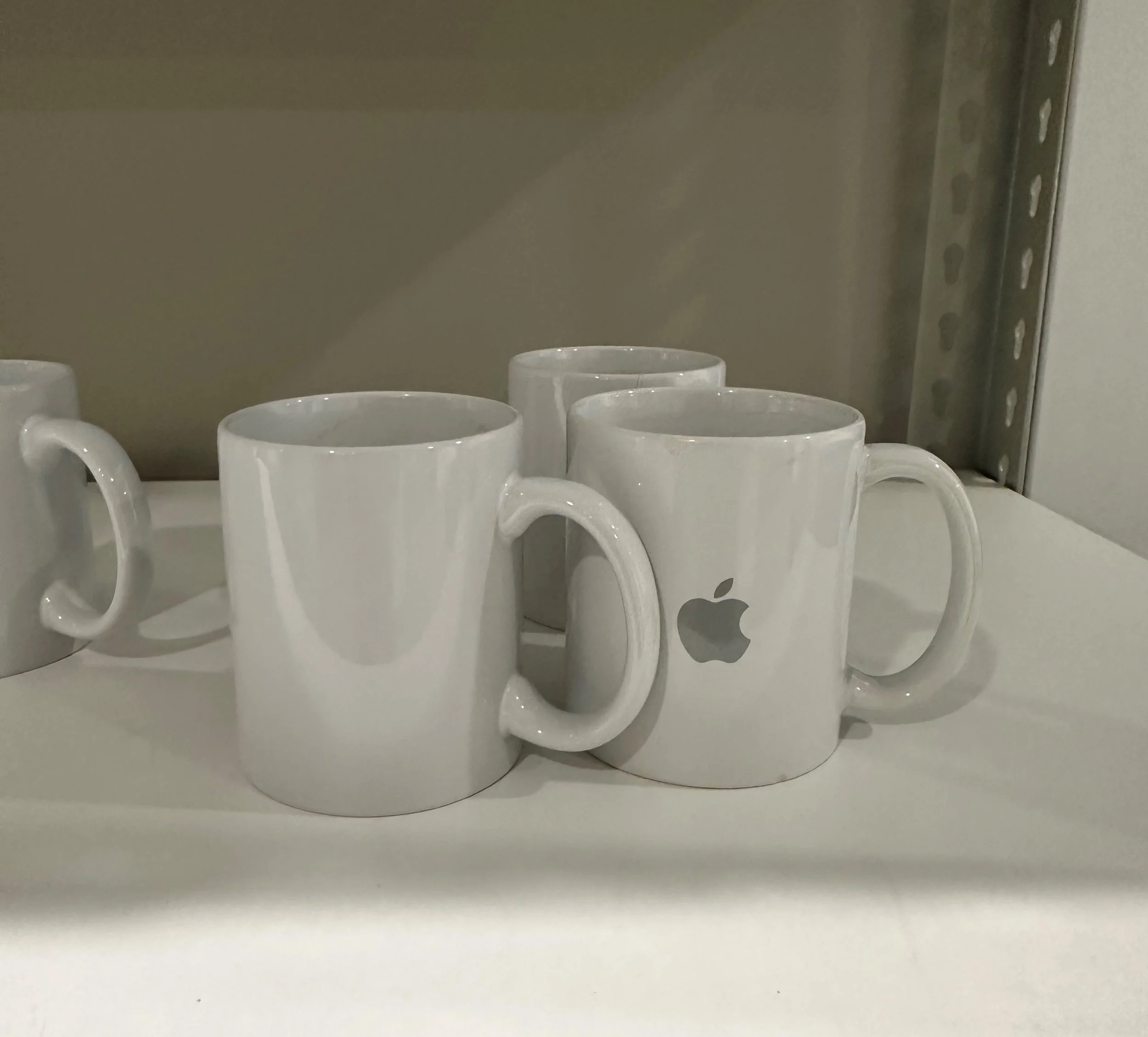 4 white mugs in shot, 1 of them with the Apple logo