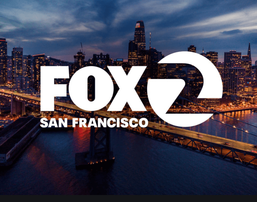 Aerial view of San Francisco skyline at dusk with illuminated buildings and bridge, over a body of water, with the FOX 2 San Francisco logo in the foreground.