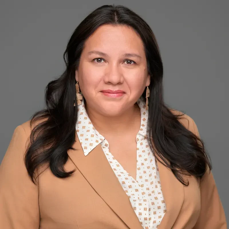 Corporate headshot of a woman in a tan blazer and patterned blouse against a grey backdrop – 204 Photography Winnipeg