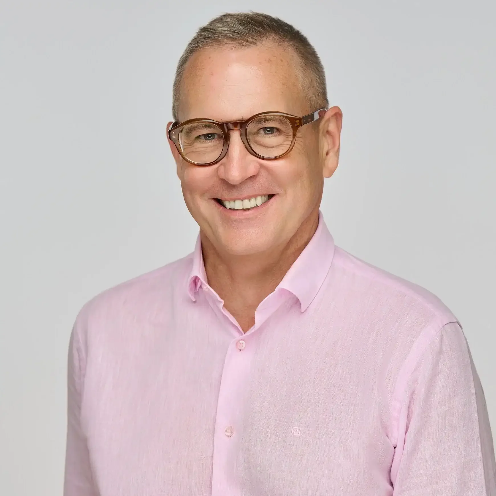 Studio headshot of a friendly businessman wearing glasses and a light pink shirt, photographed against a soft grey background in Winnipeg.