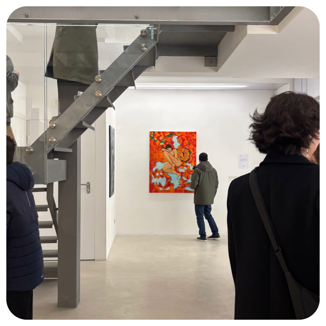 People observing artwork in an art gallery with a colorful painting of a woman surrounded by red and orange foliage on the wall.