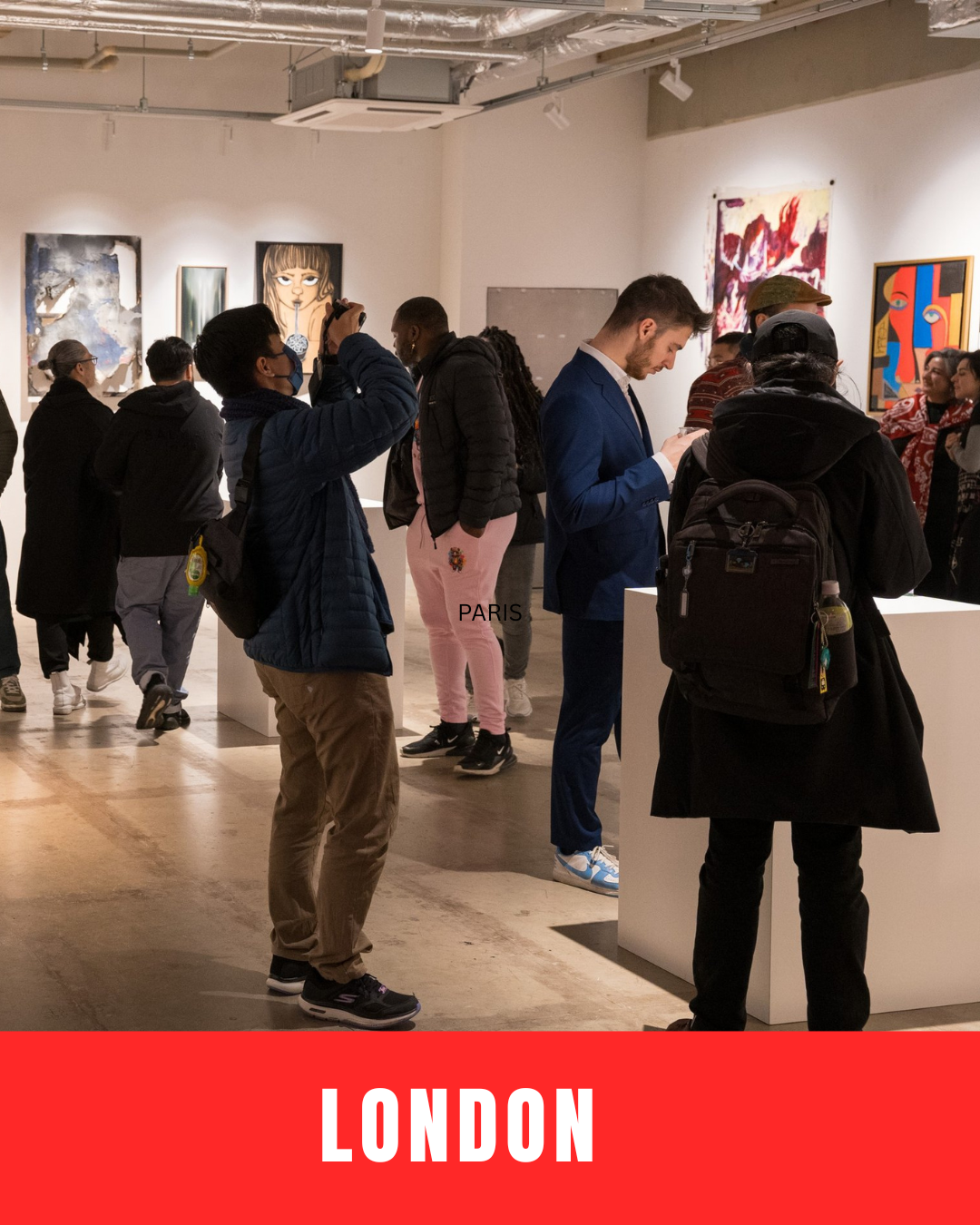 People viewing and taking pictures of artwork in an art gallery or museum with white walls and various paintings displayed.