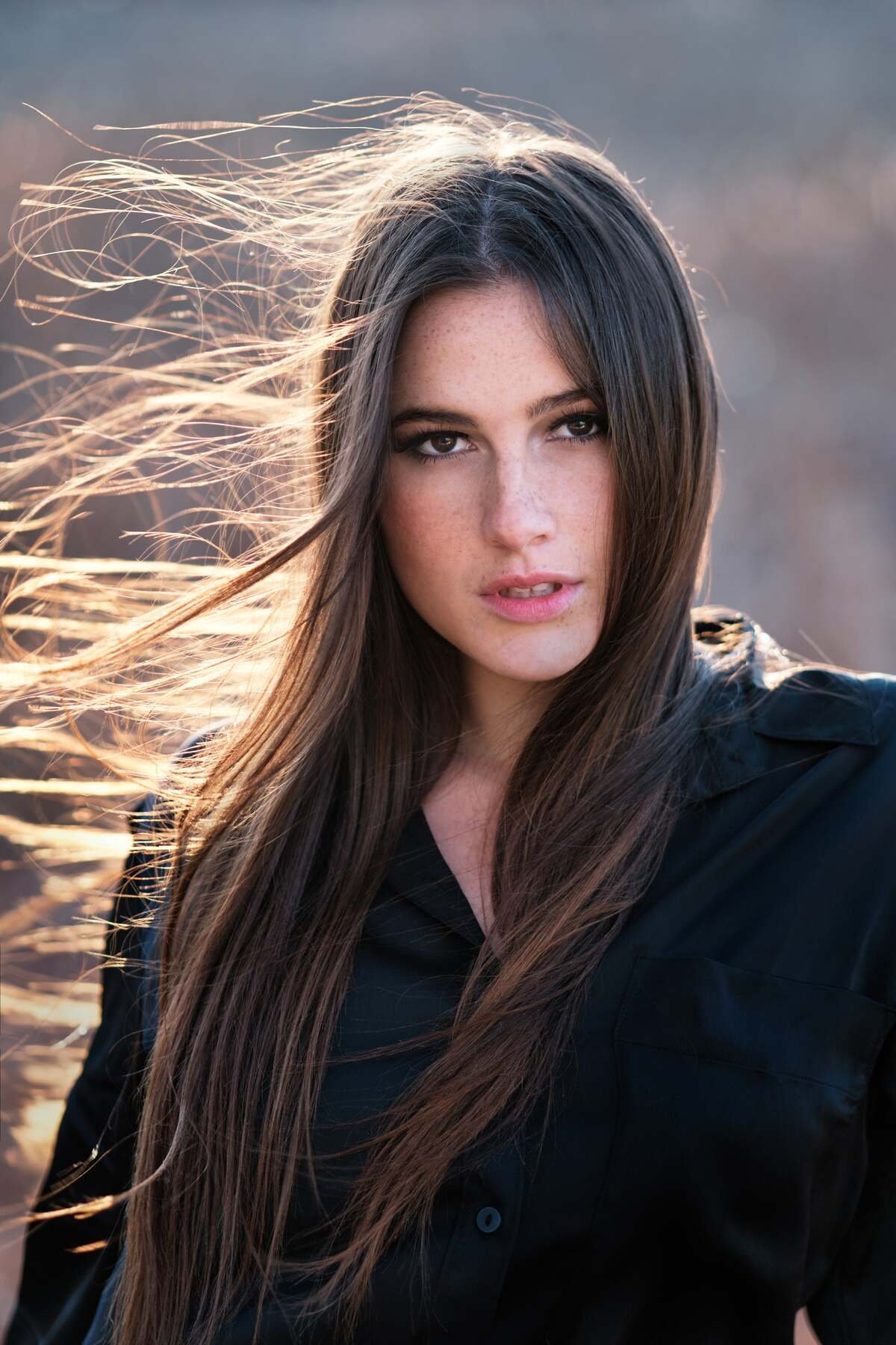 Woman with long brown hair wearing a black shirt, standing outdoors with wind blowing her hair.Photography by Henry David Photography Professional Headshots and Portraits St. Louis MO