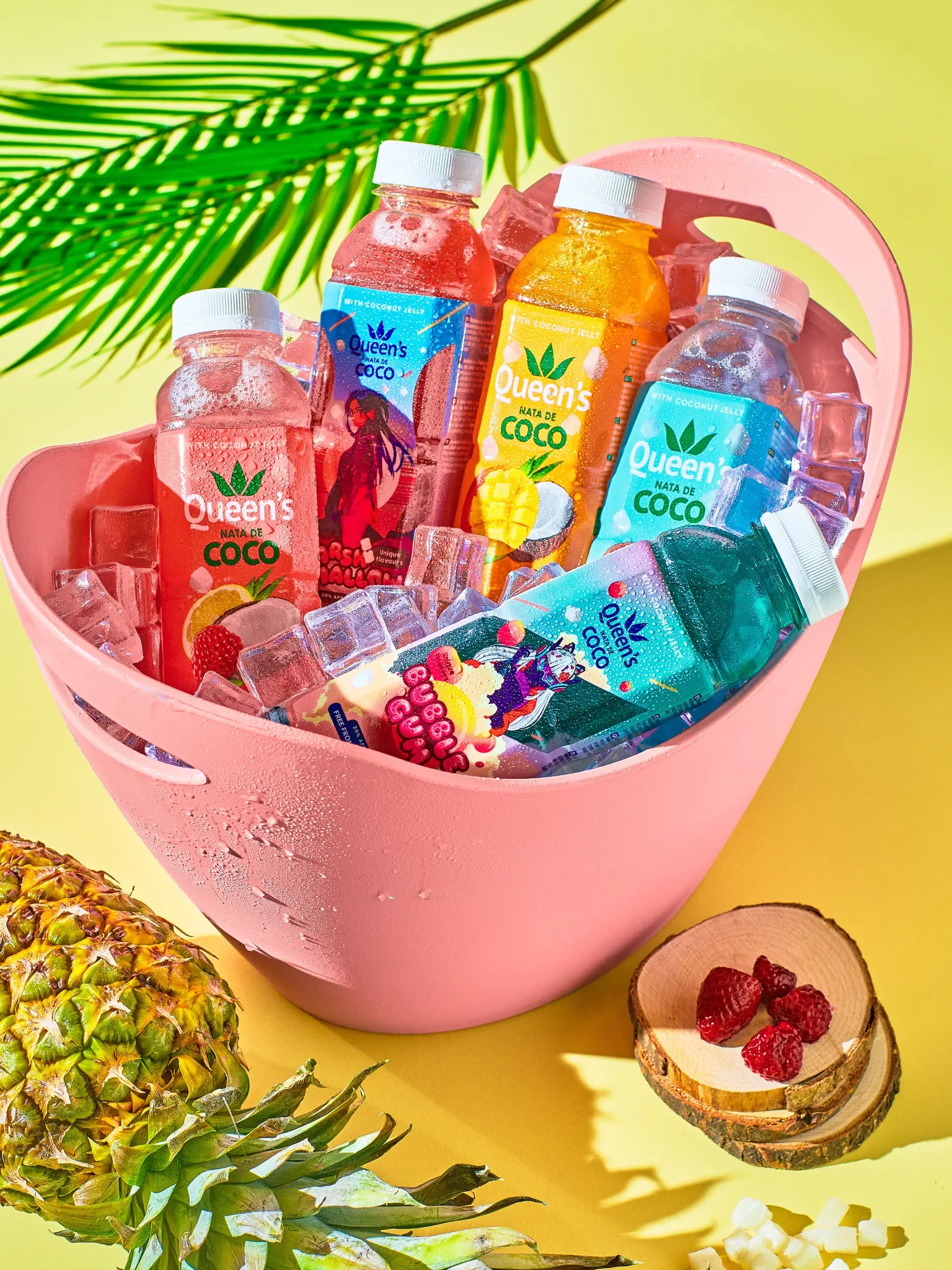 Vibrant product photography by Vasilis Geravelis με pop καλοκαιρινή αισθητική για τη σειρά αναψυκτικών Queen's Nata de Coco σε παγωνιέρα. Δημιουργική διαφημιστική φωτογραφία με έντονα χρώματα, πάγο και ανανά.