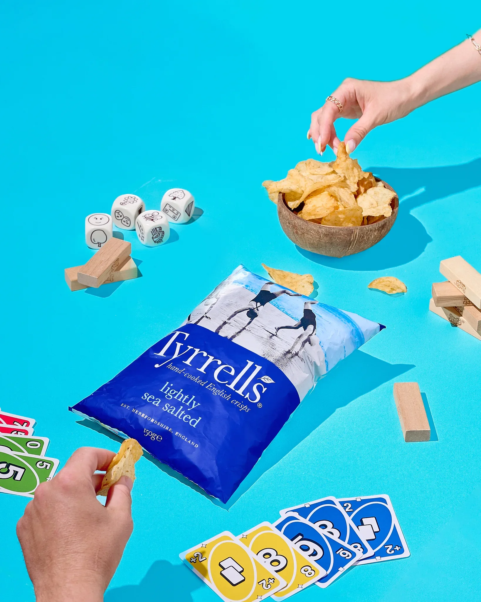 Commercial product photography by Vasilis Geravelis με στυλ color blocking για τα πατατάκια Tyrrells Crisps. Δημιουργική διαφημιστική φωτογράφιση με επιτραπέζια παιχνίδια και κάρτες σε έντονο μπλε φόντο.