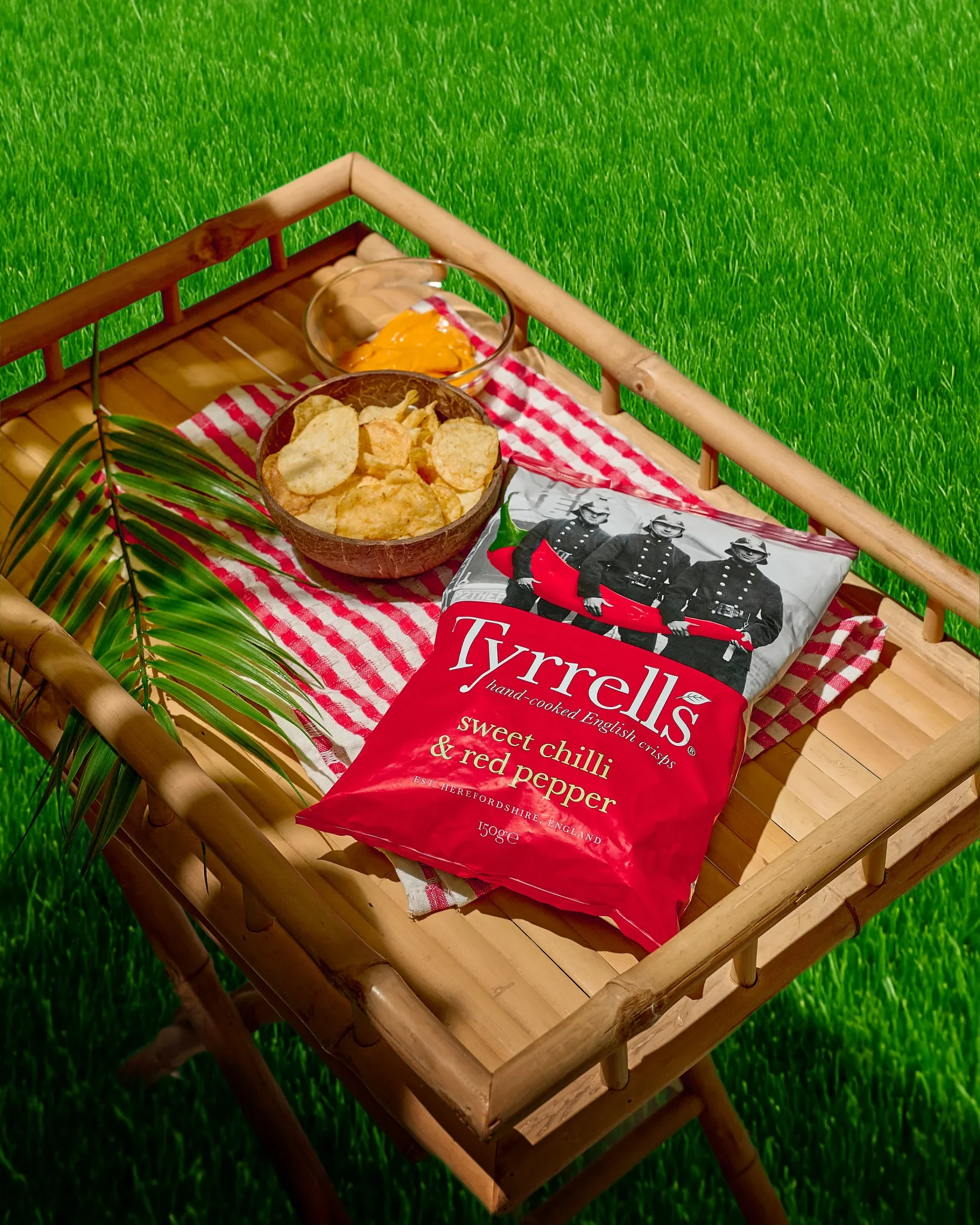 Commercial food photography by Vasilis Geravelis με concept outdoor picnic για τα πατατάκια Tyrrells Sweet Chilli & Red Pepper. Δημιουργική διαφημιστική φωτογράφιση προϊόντος σε δίσκο μπαμπού με έντονο φωτισμό και σκιές στο γκαζόν.