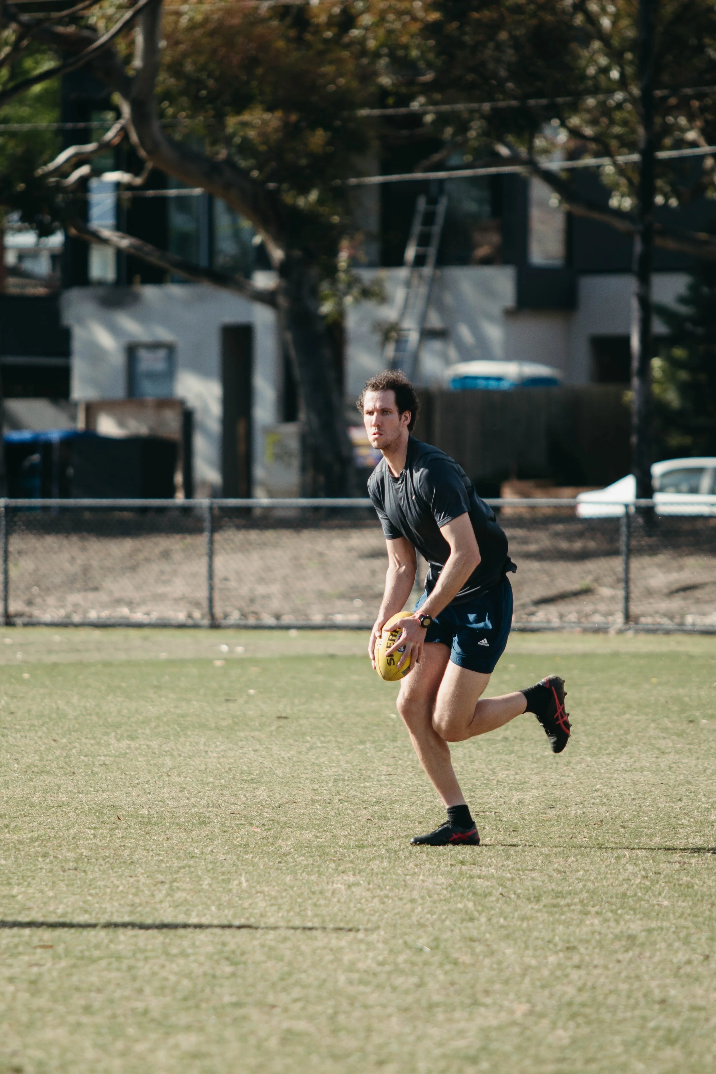 A young man in athletic clothing holding a football on a grassy field, ready to run.