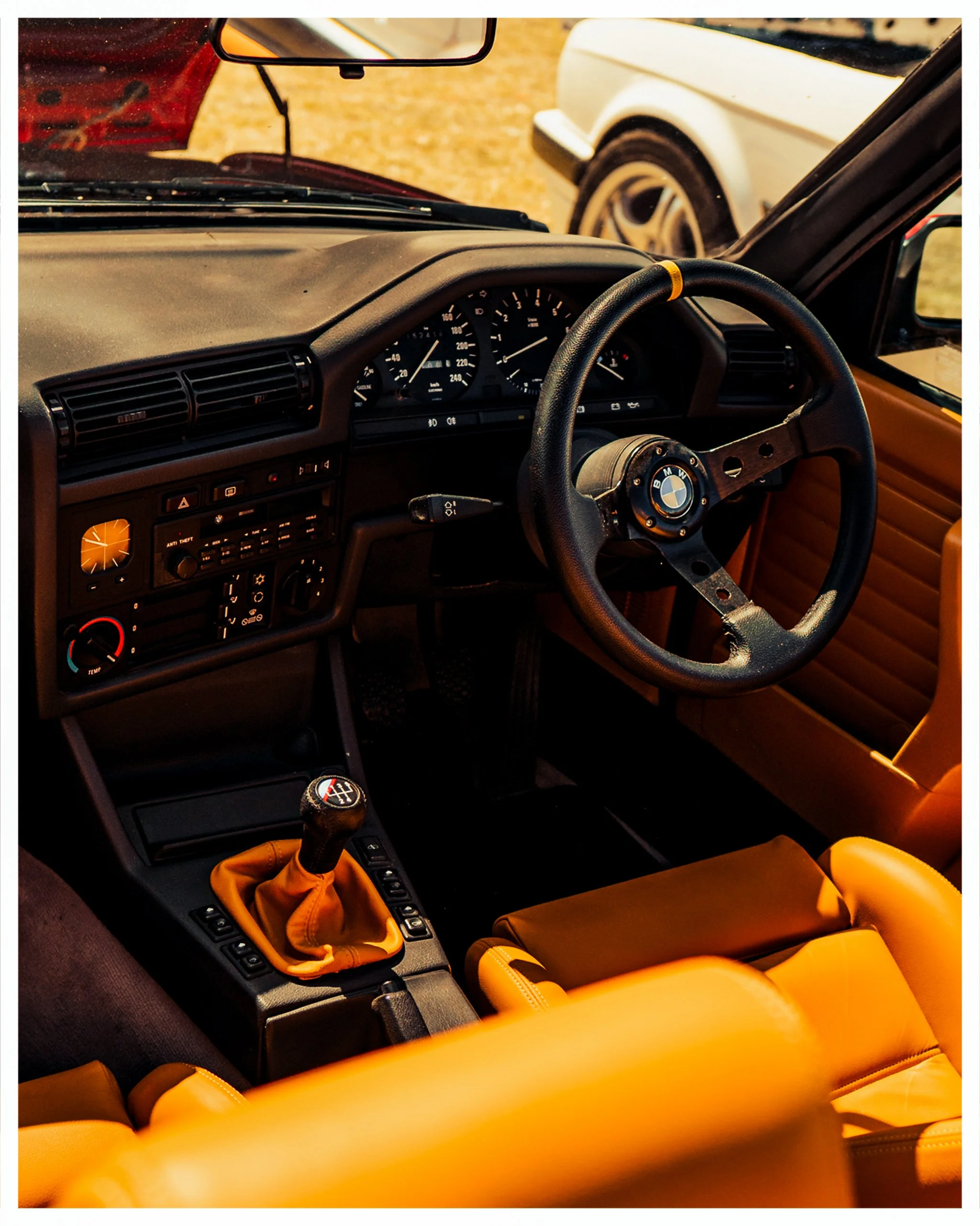 Interior of a car, showing the dashboard, steering wheel with BMW logo, and yellow leather seats. The gear shift is covered with yellow leather, matching the seats.