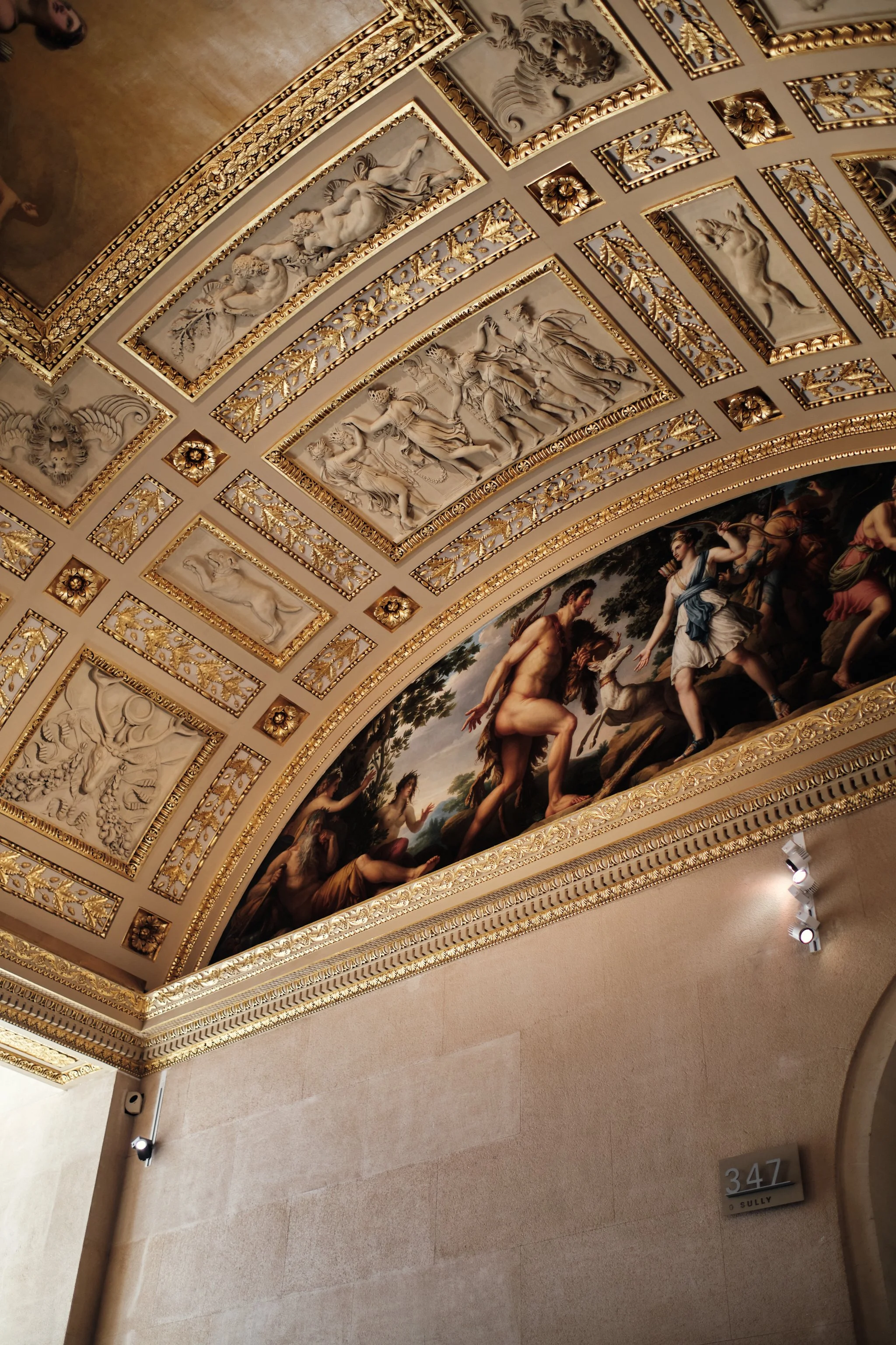 Ornate ceiling with classical sculptures and framed paintings, gold embellishments, part of a gallery or museum interior.