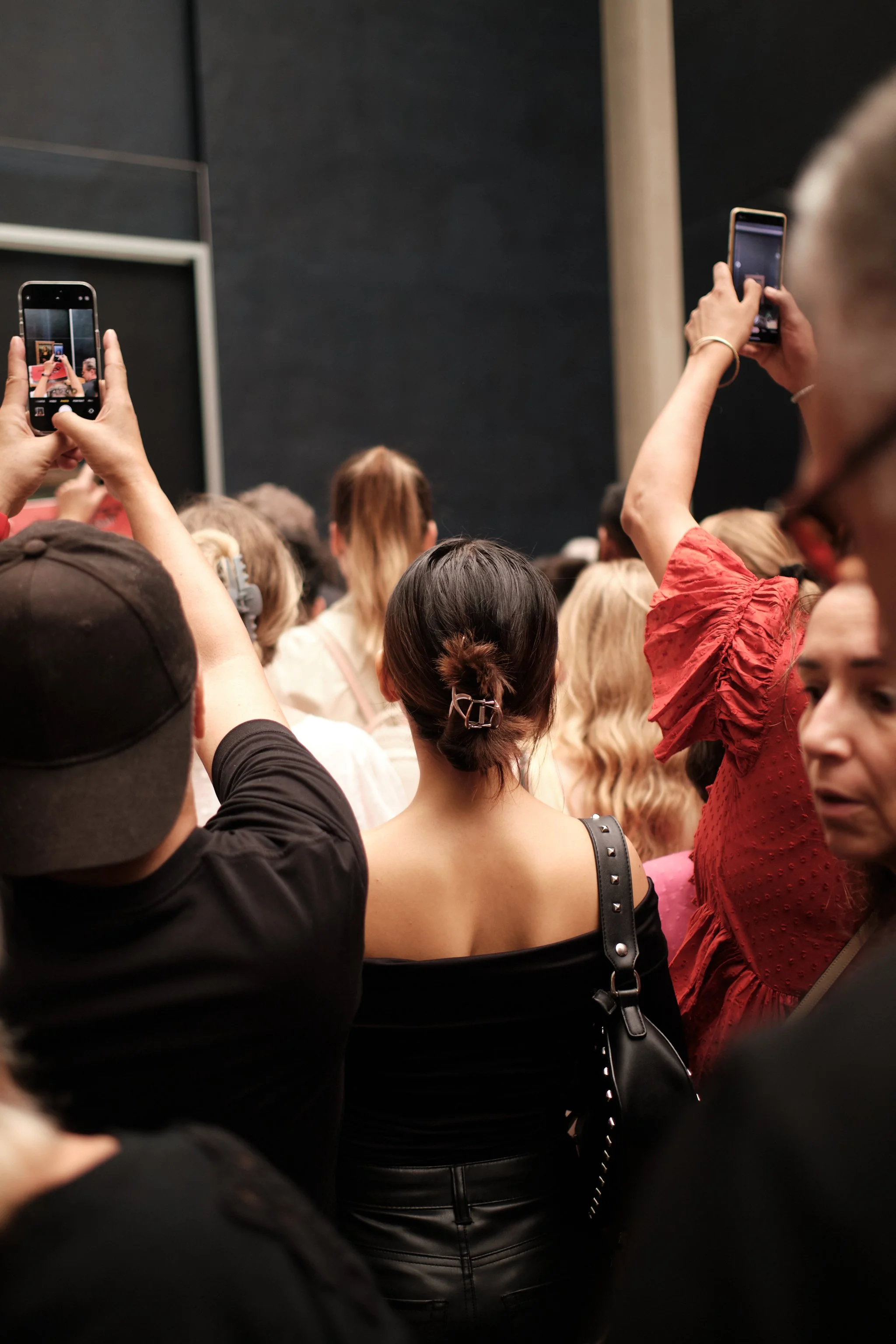 A crowd of people at an indoor event, many holding up smartphones to take pictures or record.