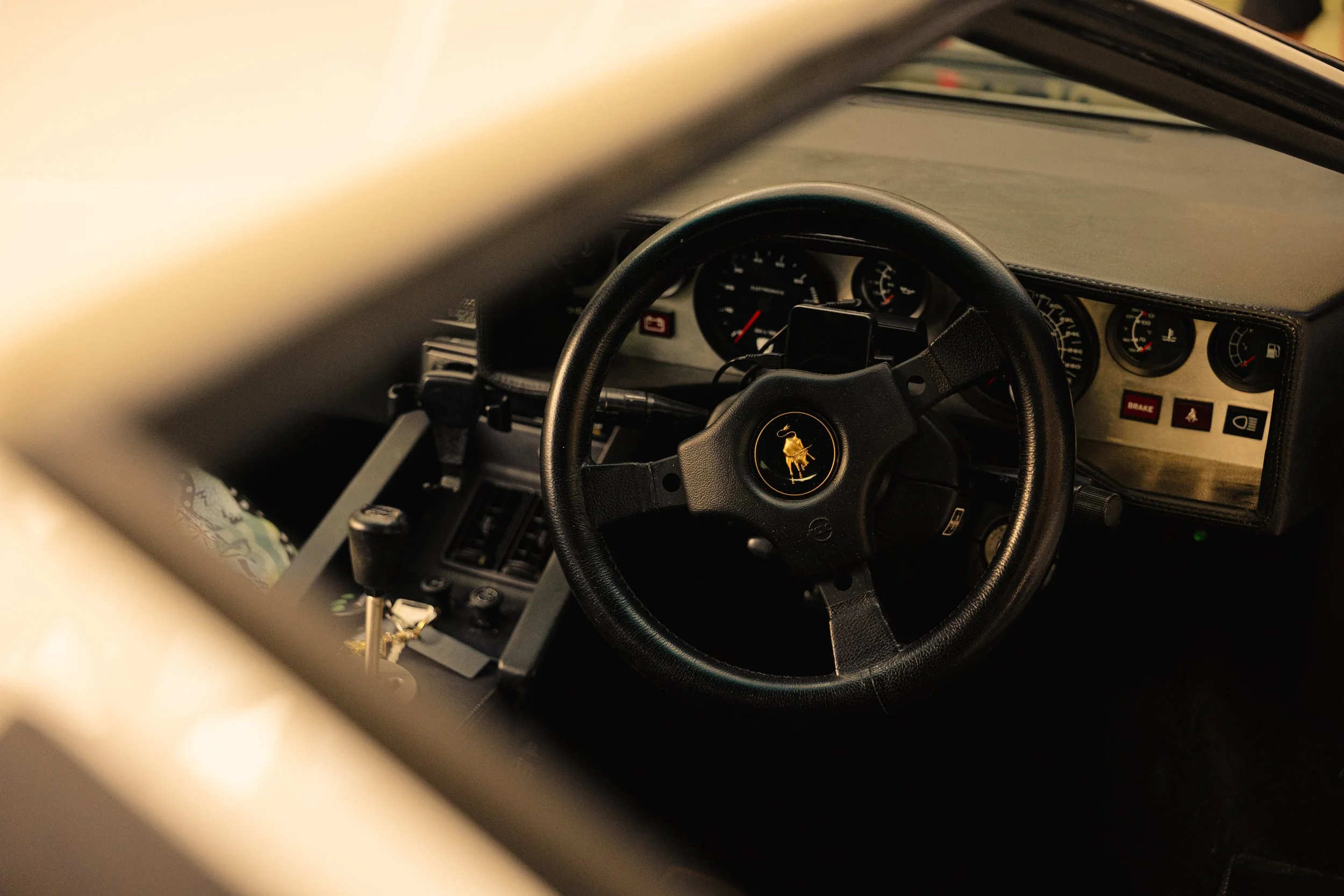 Close-up view of the dashboard and steering wheel of a vintage Lamborghini sports car, with a black steering wheel featuring the Lamborghini emblem in the center.
