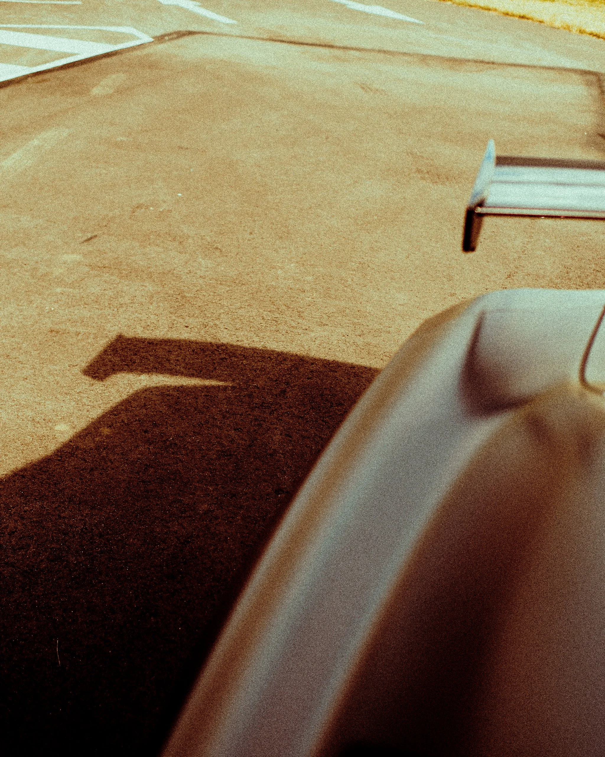 Close-up of a wooden table, part of a paper or book, and a white object, possibly a ceramic container or cup, casting a shadow on the surface.