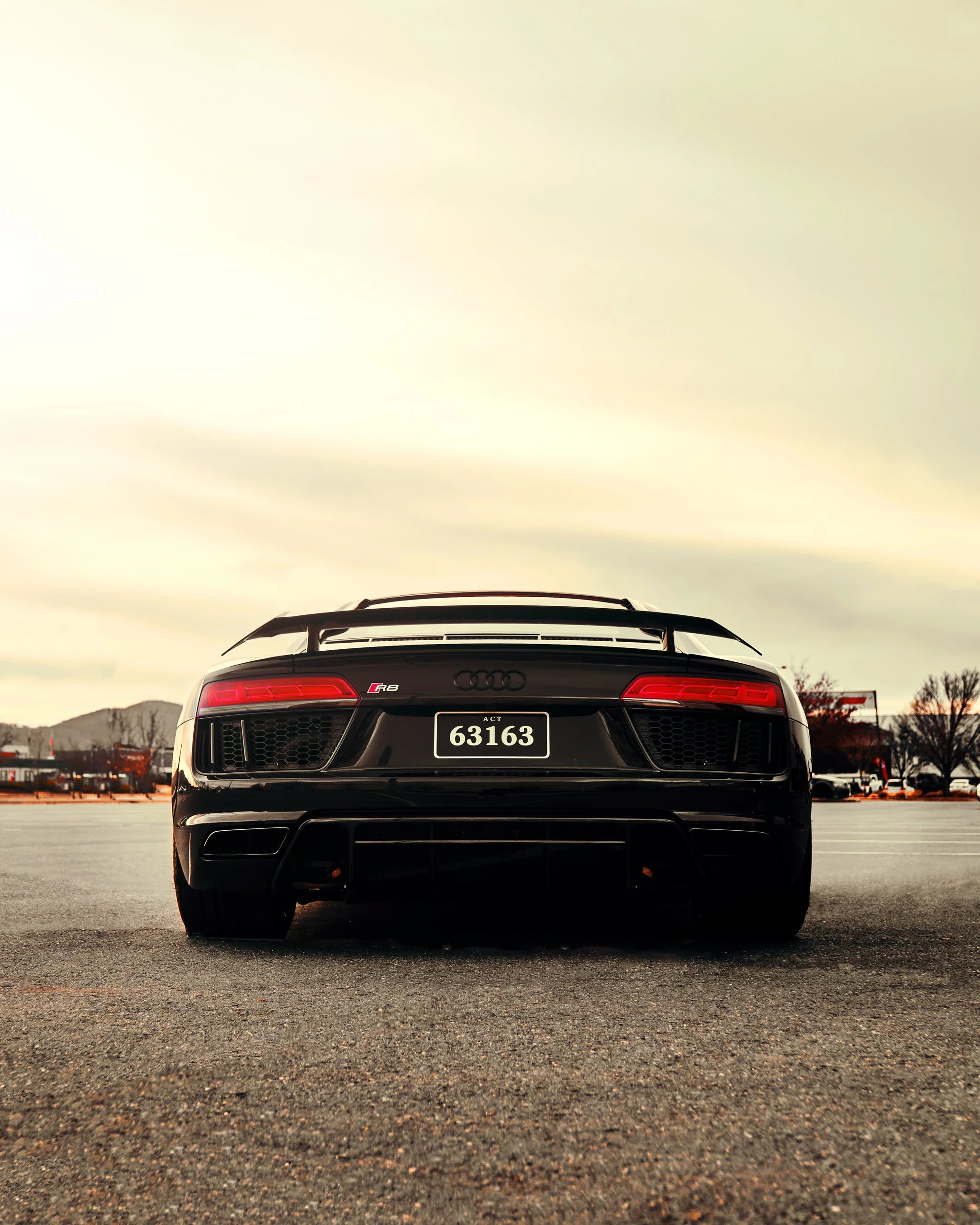 Black Audi R8 sports car in a parking lot with a gray sky background.