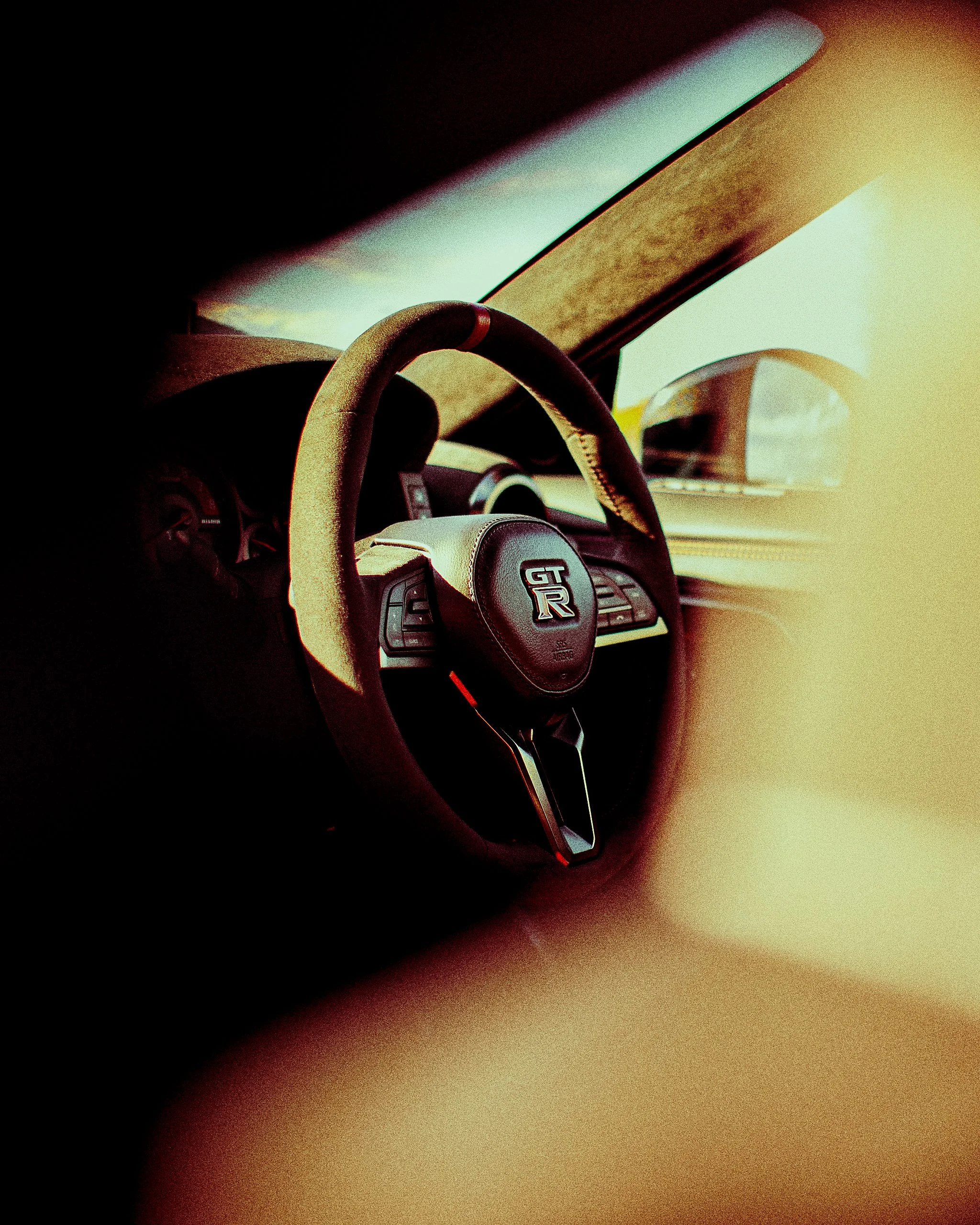 Close-up view of a Nissan GT-R steering wheel inside a car, with the dashboard in the background and sunlight casting on the interior.