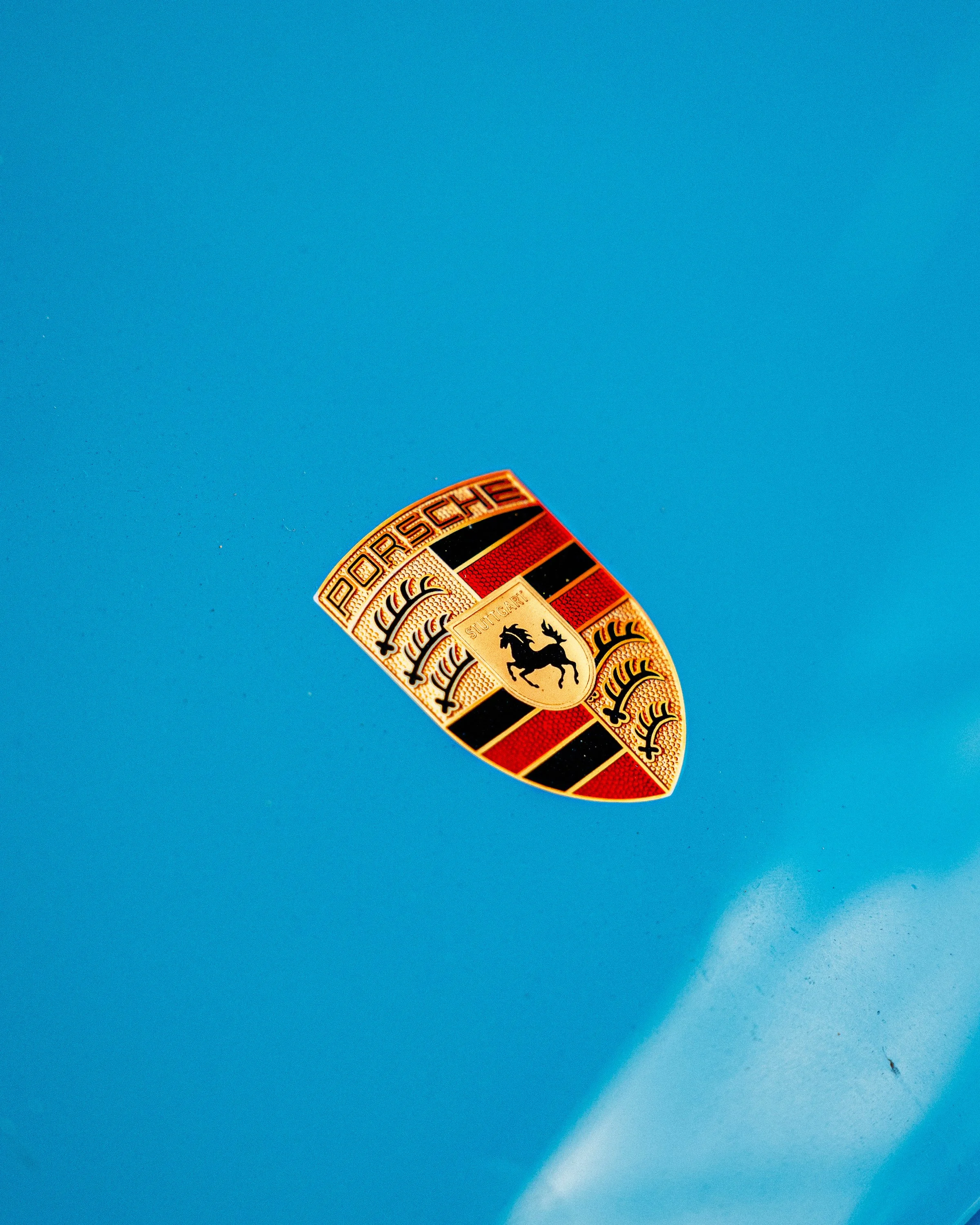 Close-up of a Porsche emblem sticker on a blue surface, with other similar stickers partially visible.