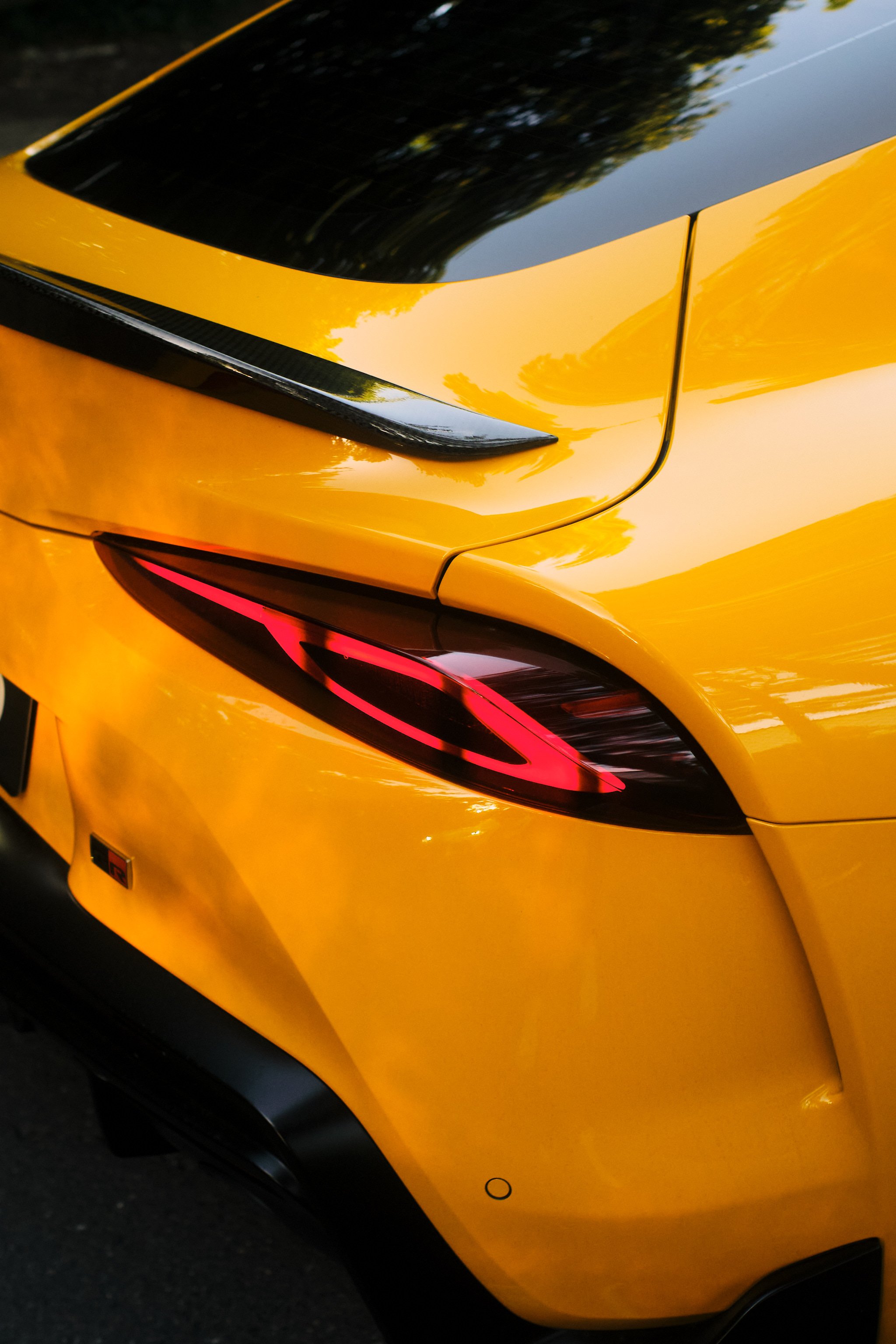 Close-up of the rear corner of a yellow sports car, showing the tail light and part of the trunk with a black trim detail.