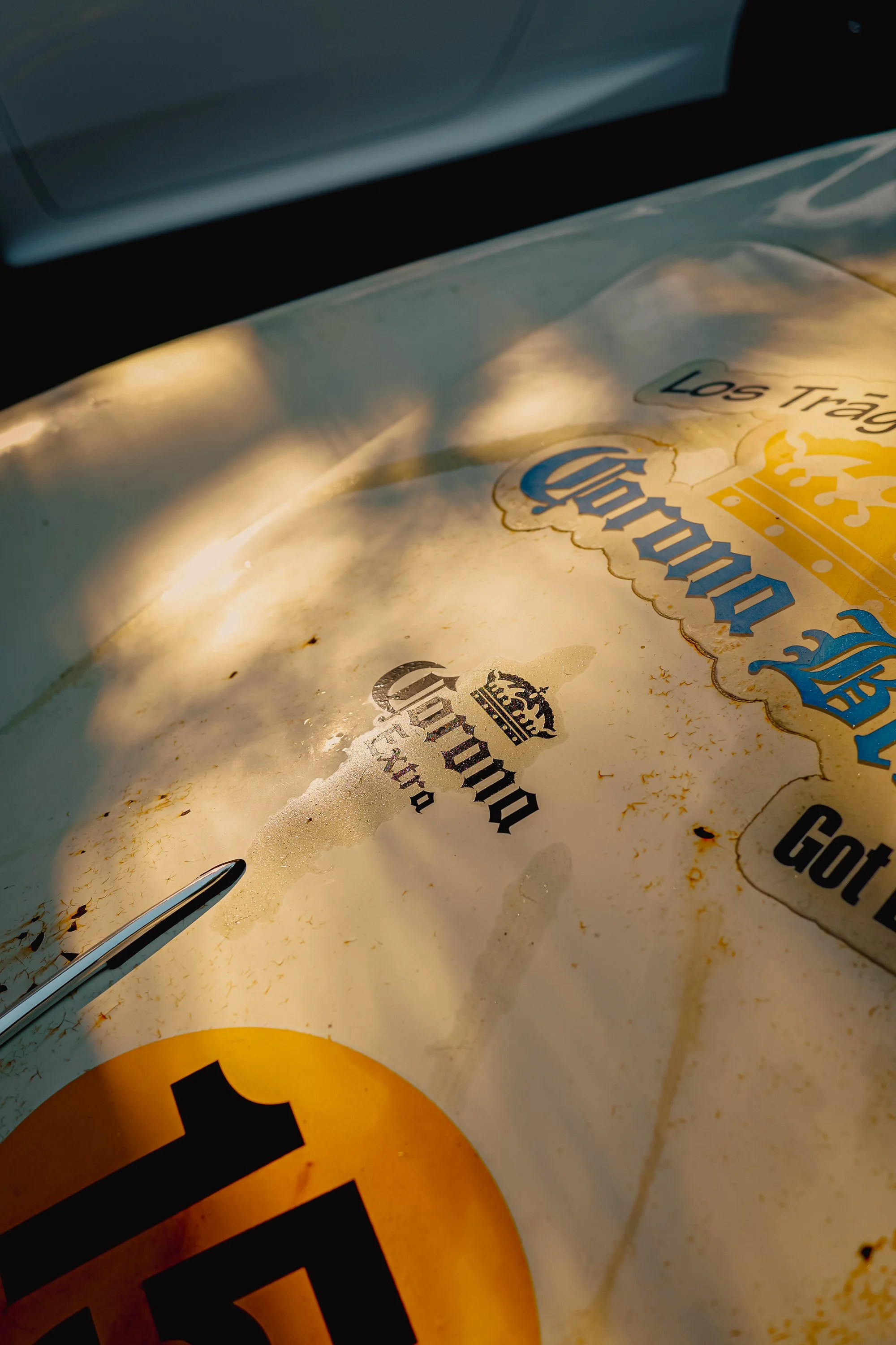 A close-up of a paper cup with a partially peeled sticker showing the word 'Corona' and the phrase 'Los Tragos' visible, with a yellow color and black text, and a black and yellow globe logo at the center.