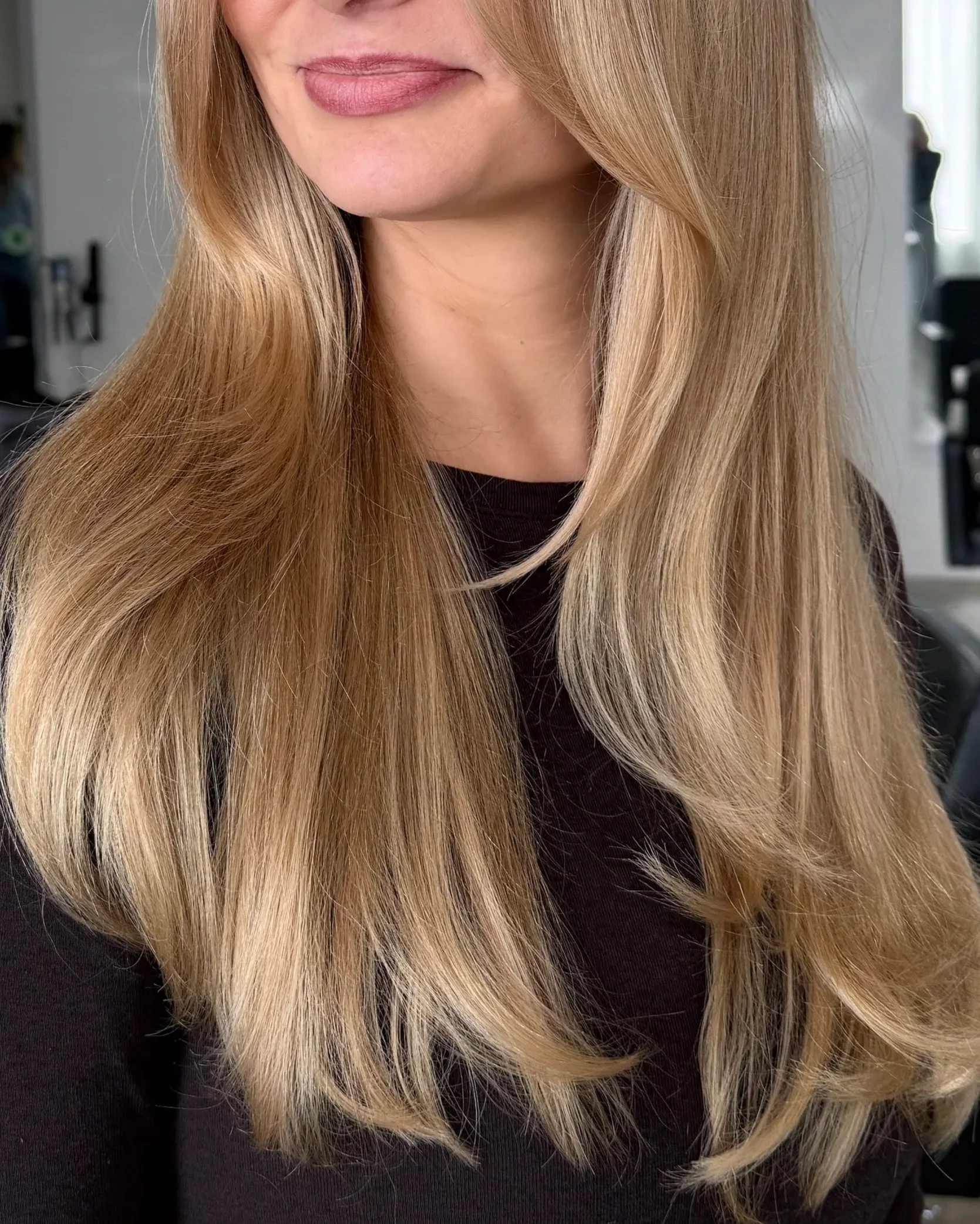 Close-up of a woman's face and long blonde hair, wearing a black top, with a blurred background.