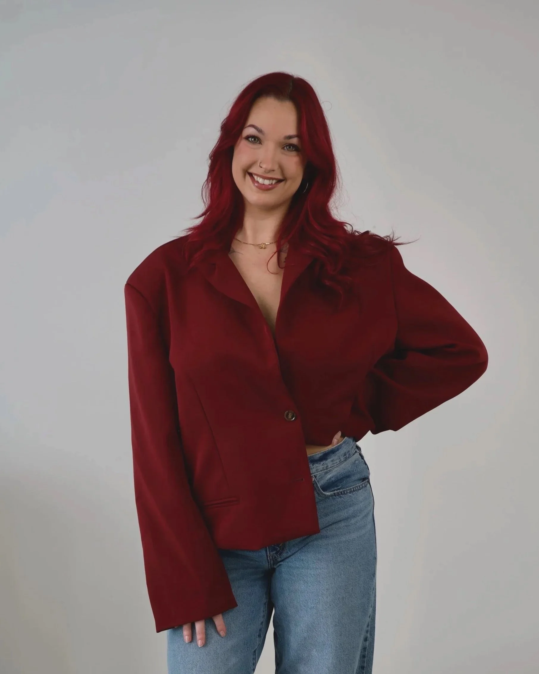 A woman with shoulder-length wavy hair wearing a gray sleeveless vest and a black skirt, standing against a plain light gray background.