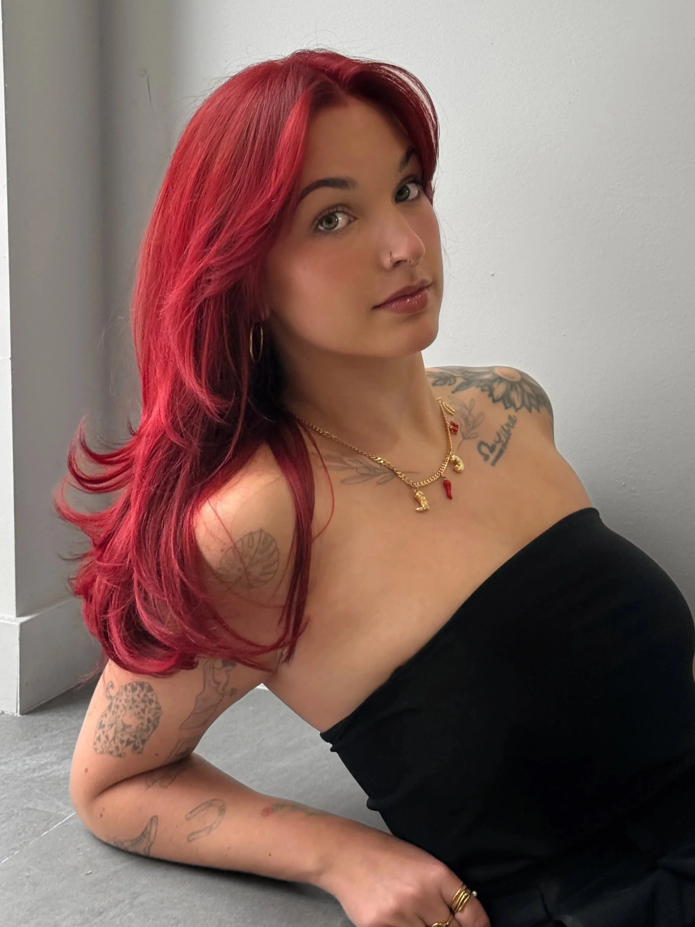 A woman with shoulder-length wavy hair wearing a gray sleeveless vest and a black skirt, standing against a plain light gray background.