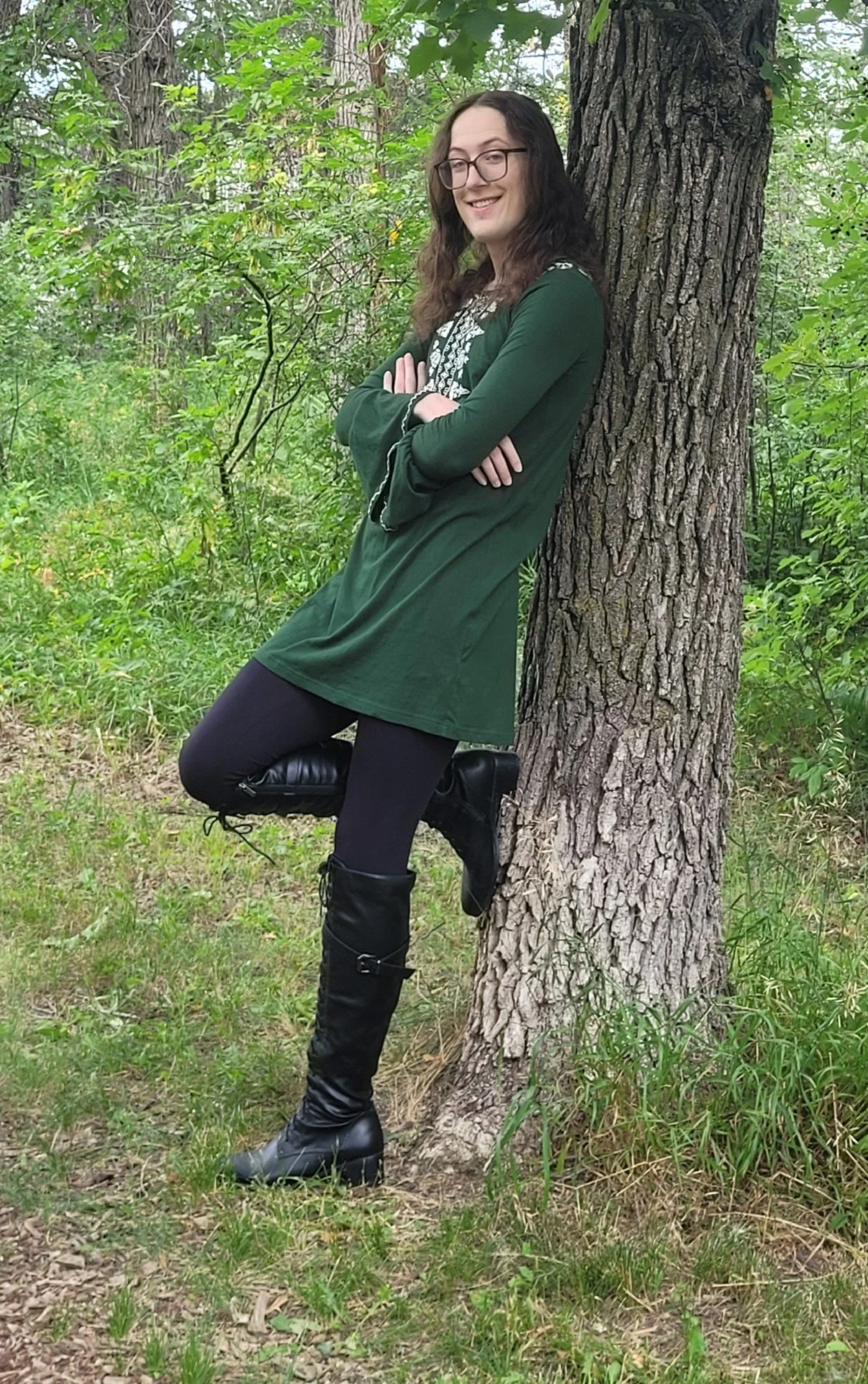 an image of cory wearing a green smock, leaning against a tree