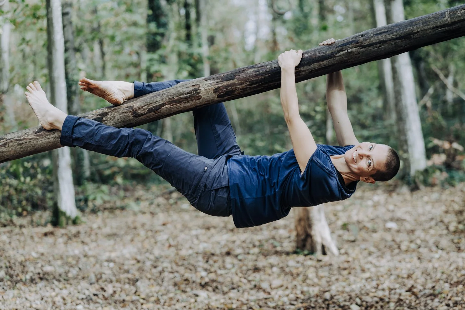 Frau hängt an einem Baumstamm und lacht in die Kamera