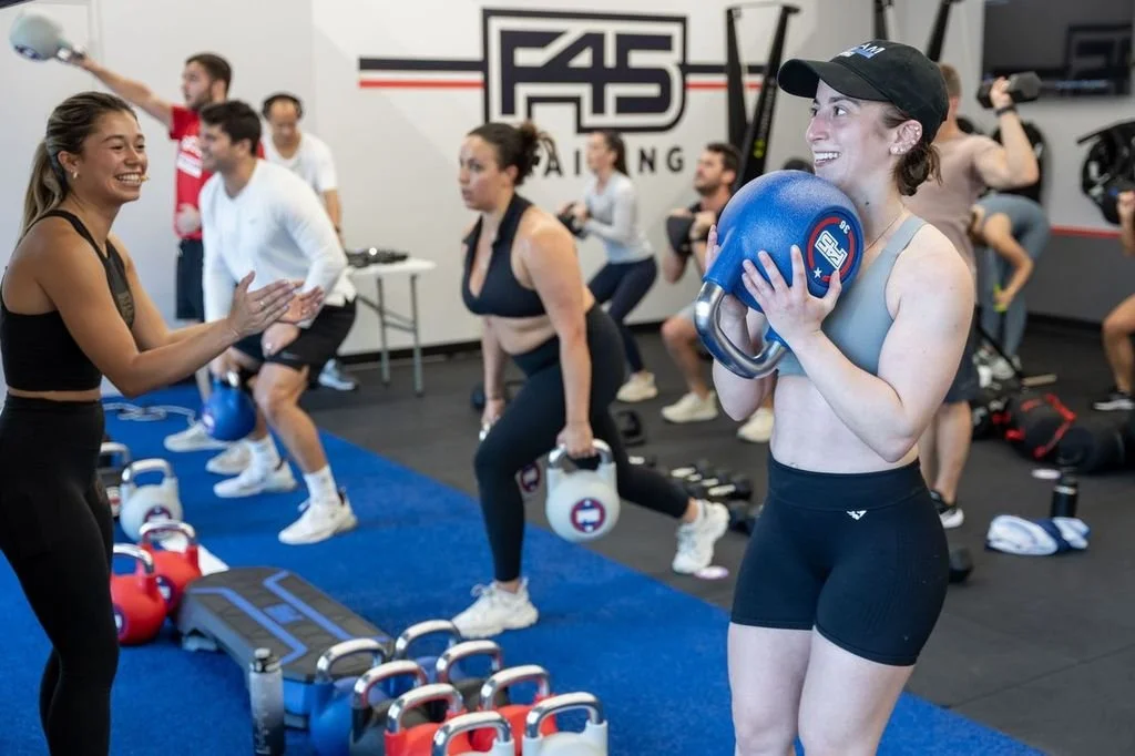 Coach Christina cheers on Luca as she front squats a kettlebell at the F45 Training North End Grand opening class