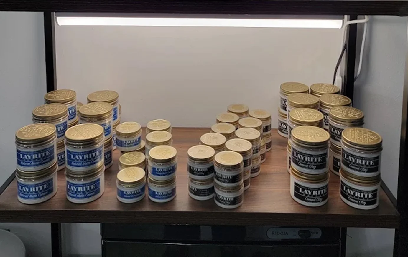 Layrite Natural Matte Cream and Cement Clay tubs on the shelf at The Bus Stop Barbershop in SoMa, San Francisco.