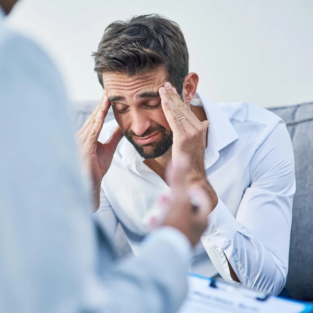 Man appears distressed holding his head during a consultation with a doctor.
