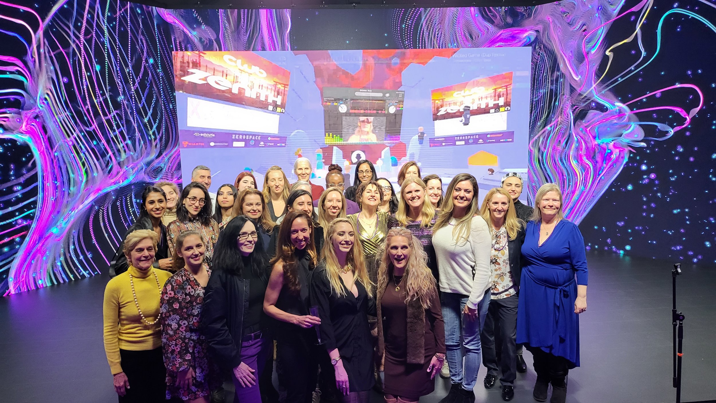 A group of people posing for a photo in front of a digital, colorful backdrop at a club or event.