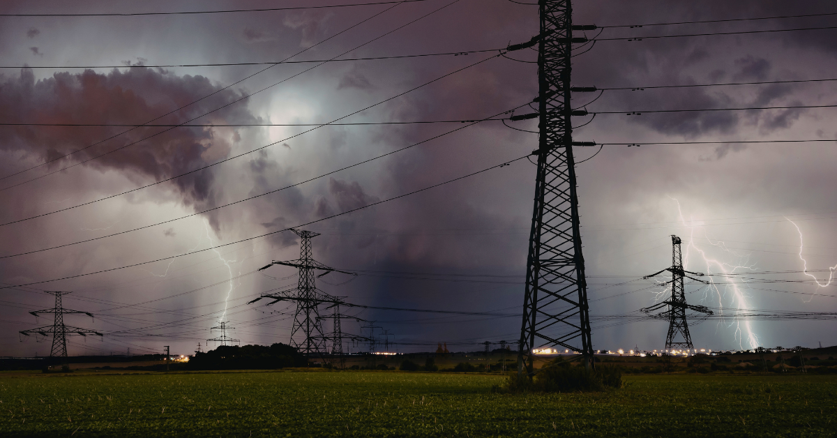 Lightning strikes near electrical transmission towers during a storm illustrating power surge risk to homes