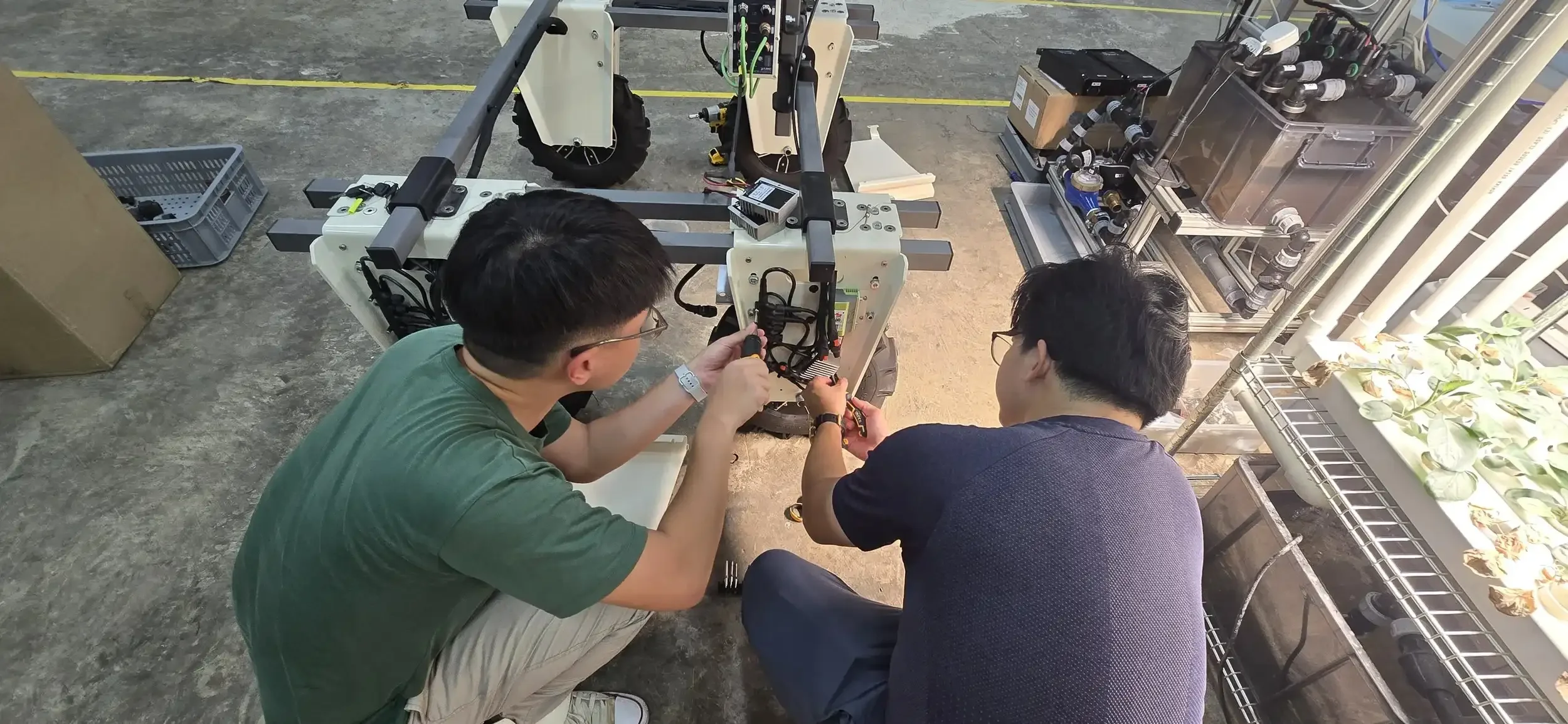 Two engineers working on a robot with a robotic arm in an industrial setting, surrounded by various mechanical and electronic components.
