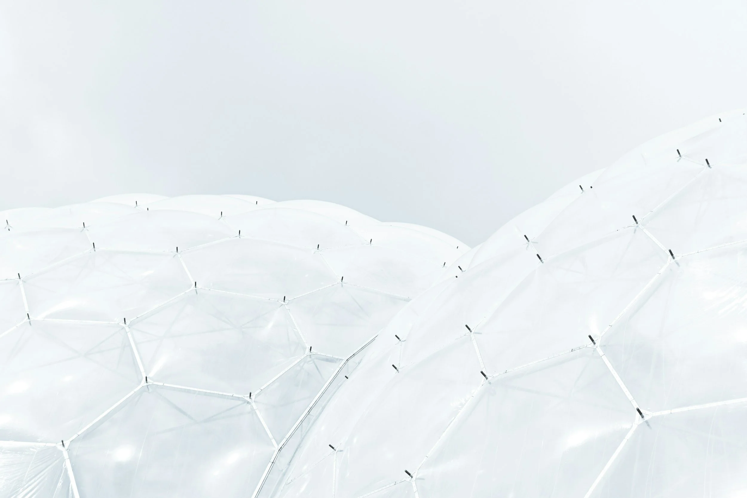 Close-up view of a modern, white geodesic dome structure made of interconnected panels with black fasteners, set against a cloudy sky.
