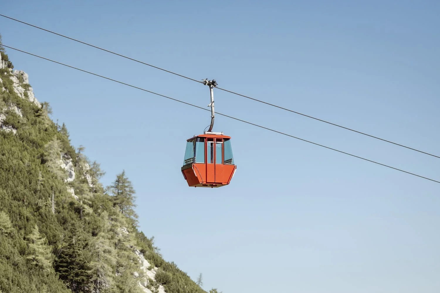 A red gondola rides up the mountain against a blue sky