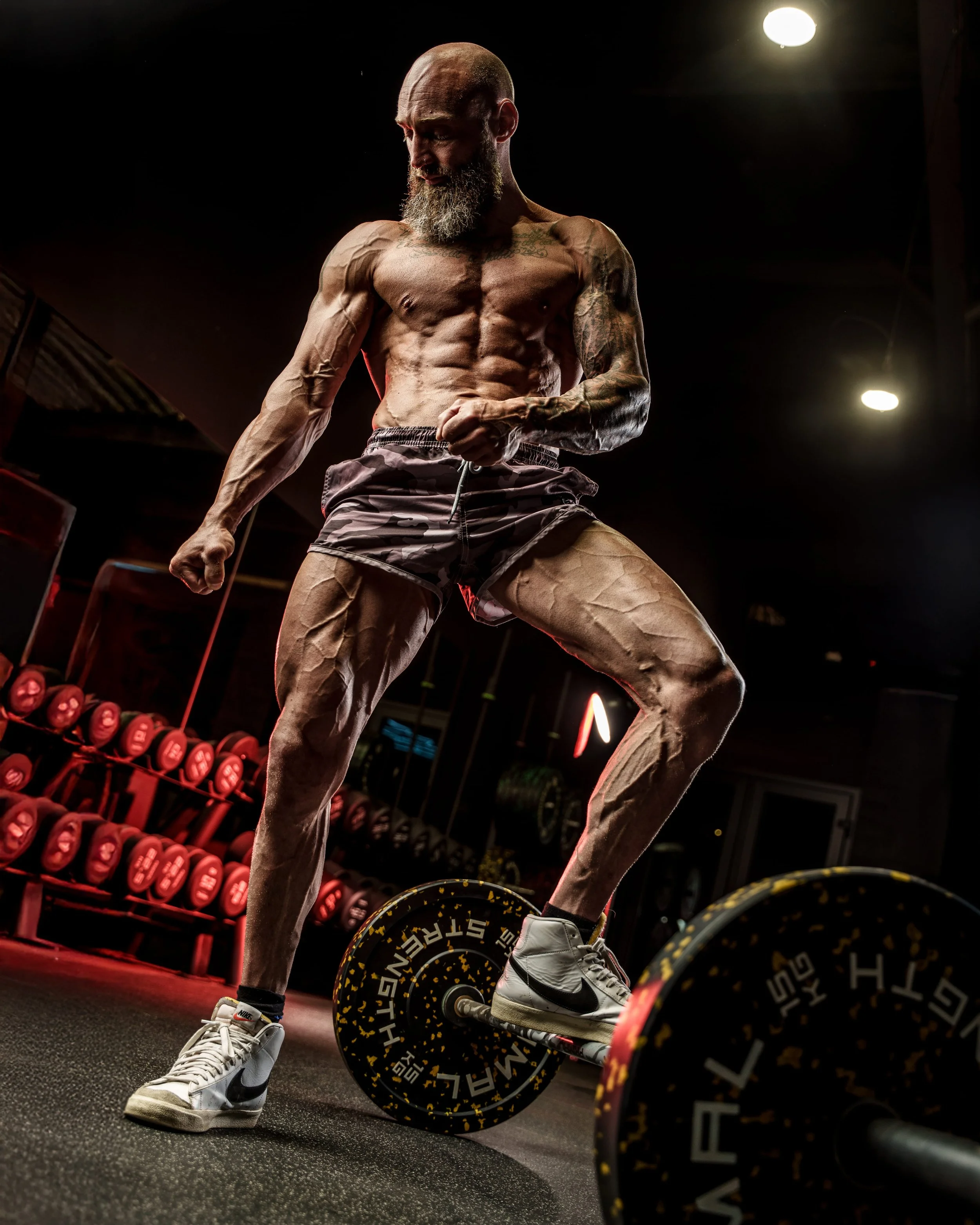 Bodybuilding photoshoot of a mature muscular athlete deadlifting a barbell in a gym, highlighting strength, power, and physique conditioning.