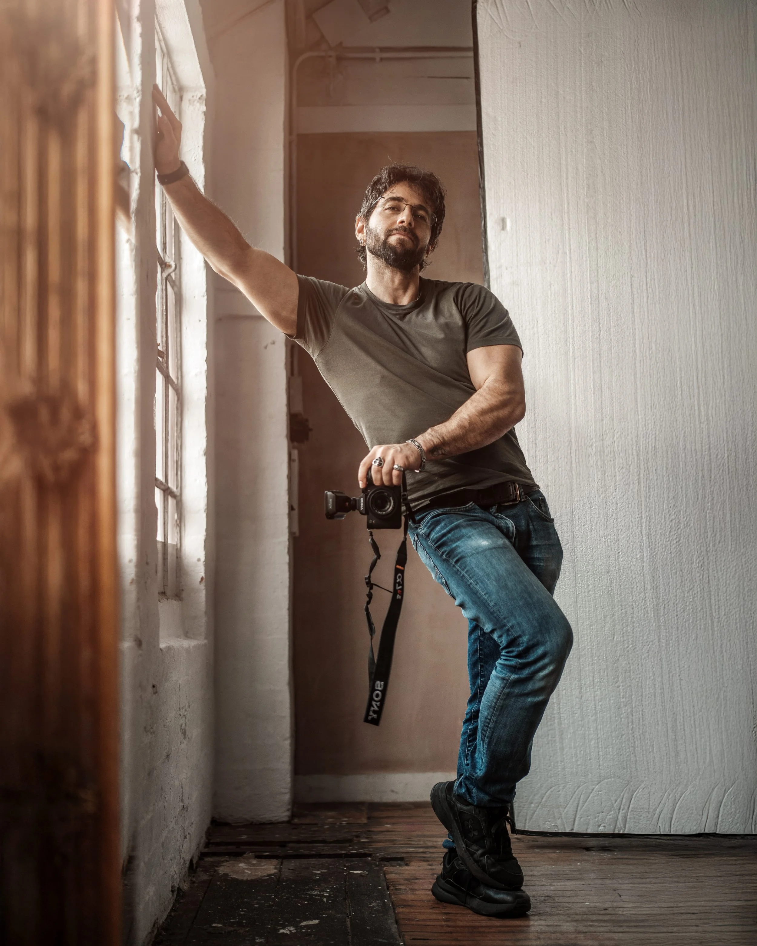 Behind the scenes editorial portrait of photographer Mak Freeman holding a camera in a private studio, demonstrating a relaxed confident presence during a client photoshoot in the UK.