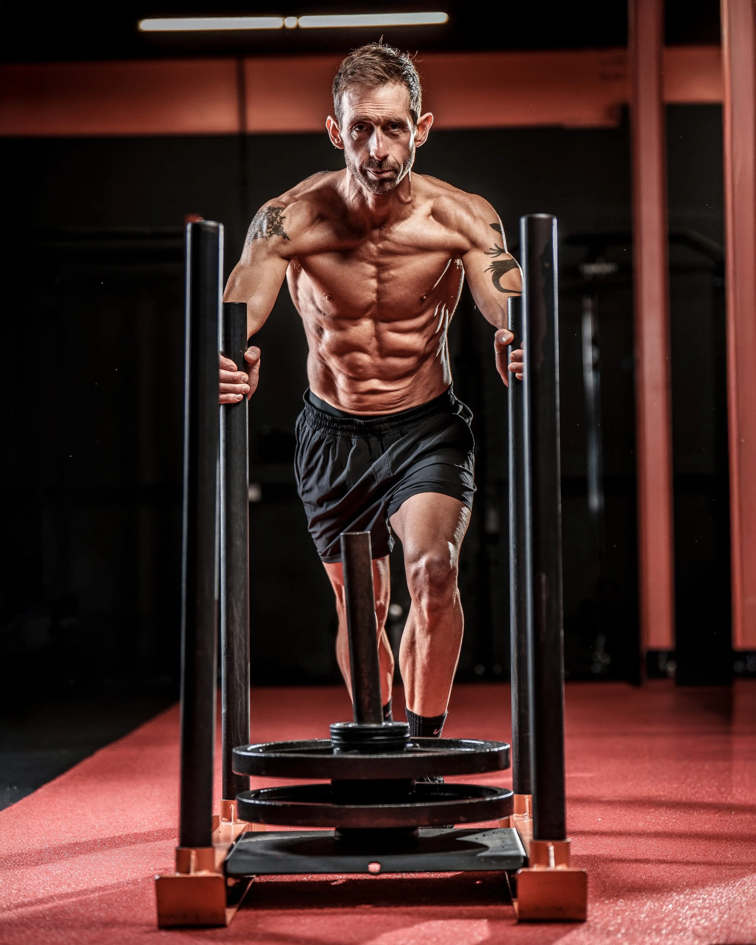 Bodybuilding photoshoot of a lean muscular man pushing a weighted sled in a gym, captured during an intense fitness photography session.