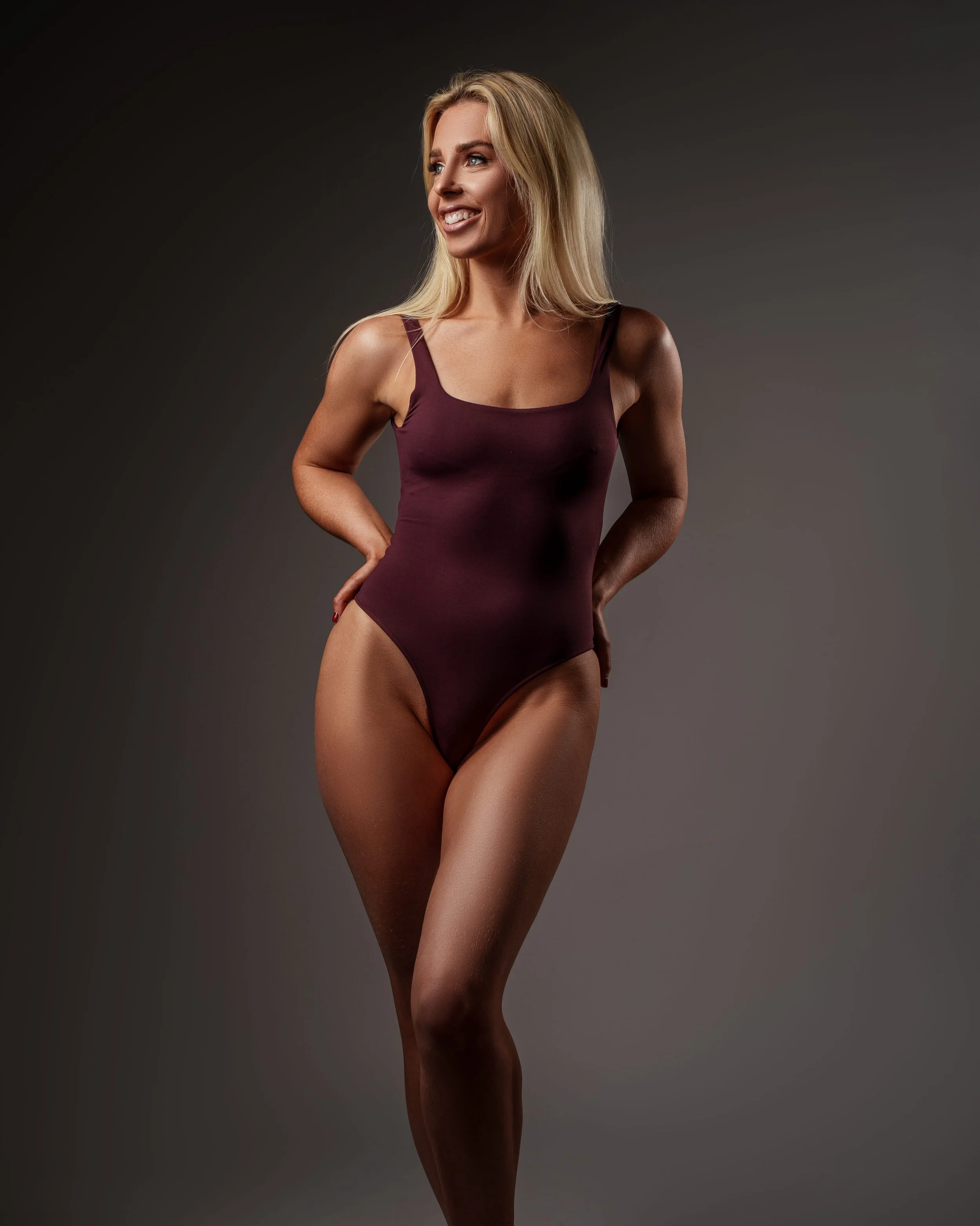 Editorial studio portrait of a confident woman in a minimalist bodysuit, shot in a clean studio setting with strong lighting and a magazine style finish in the UK.